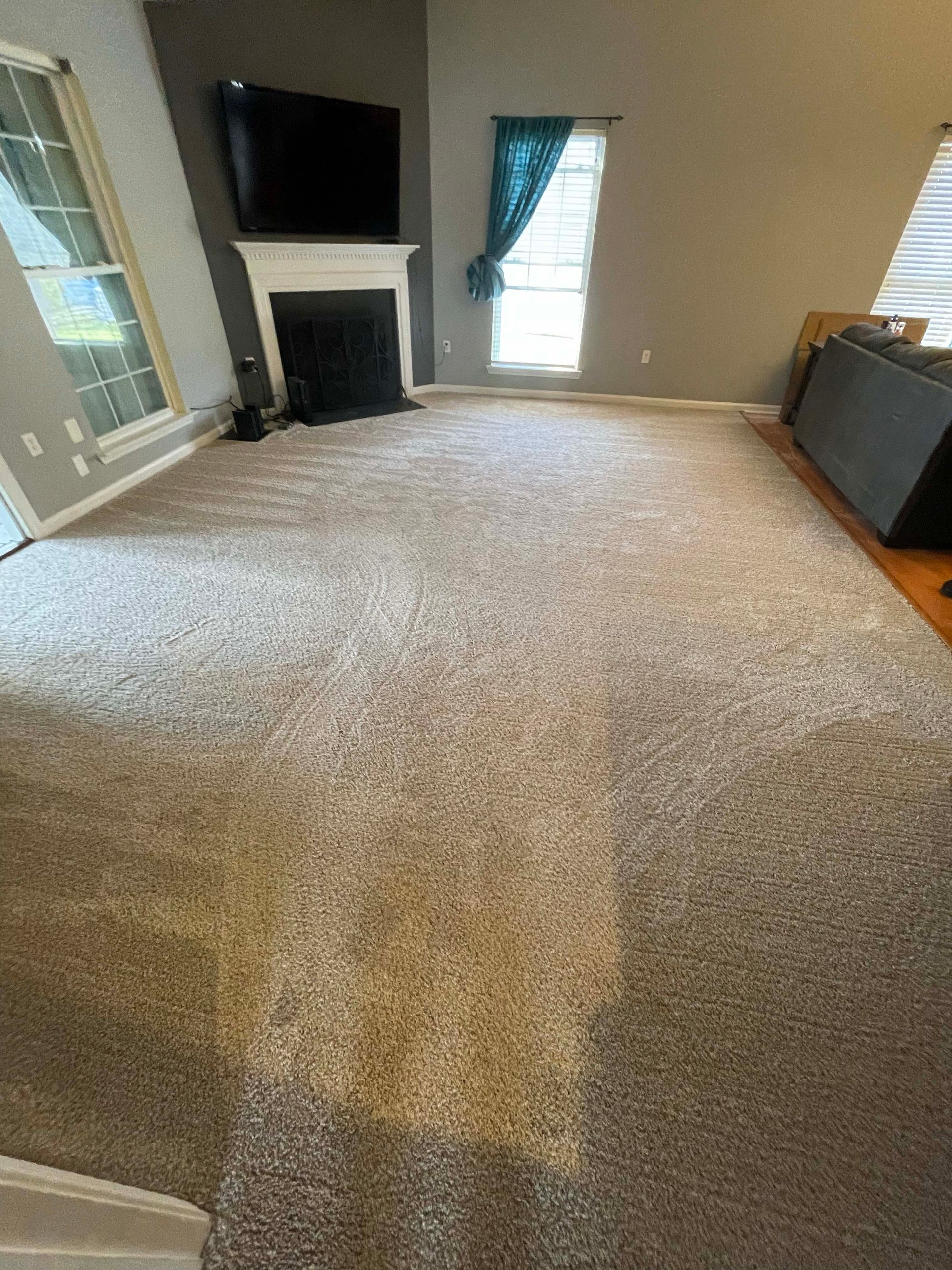 Large living room with beige carpet, a fireplace, and a TV.