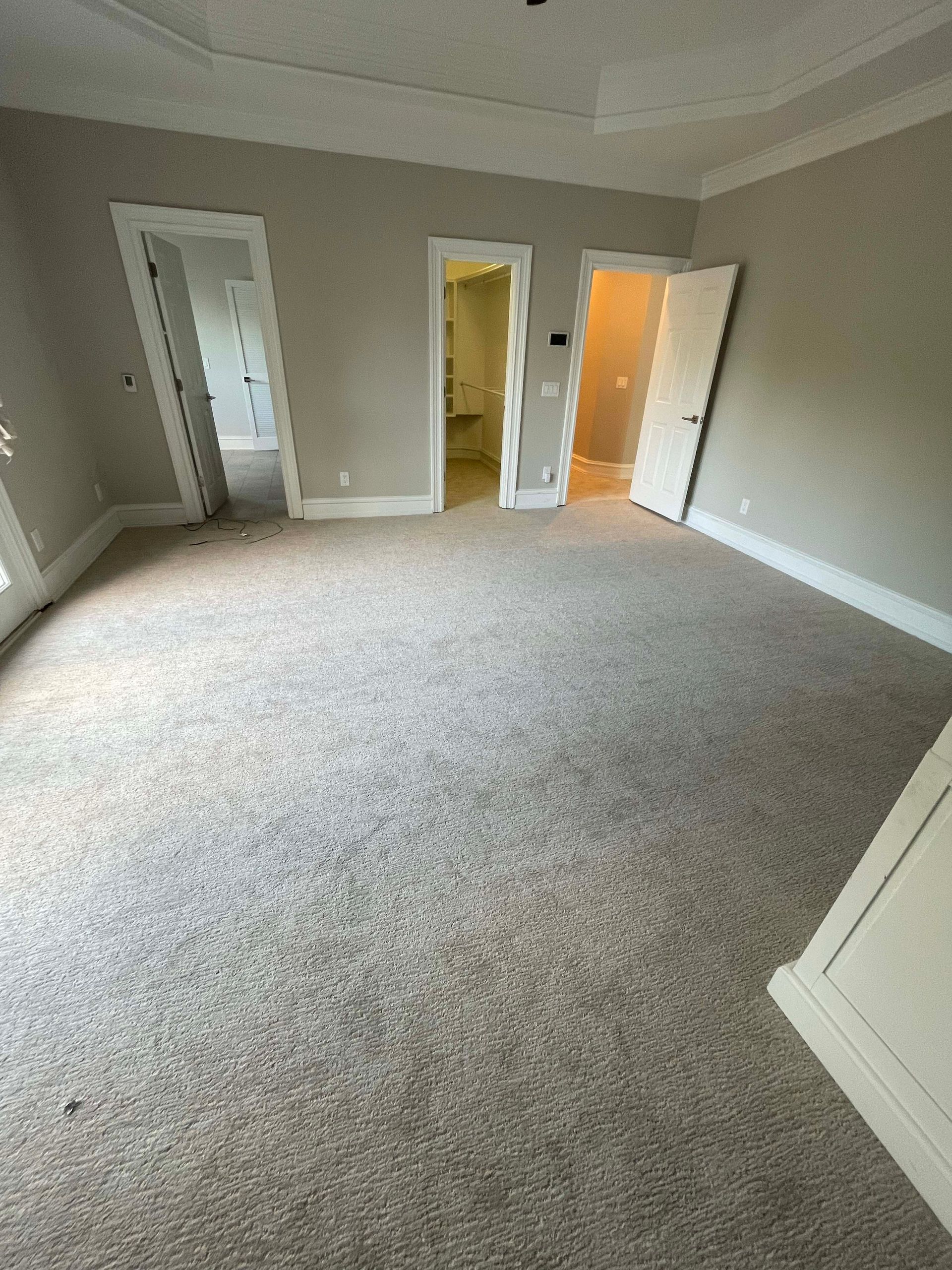 Empty bedroom with tan carpet, beige walls, and three doorways.