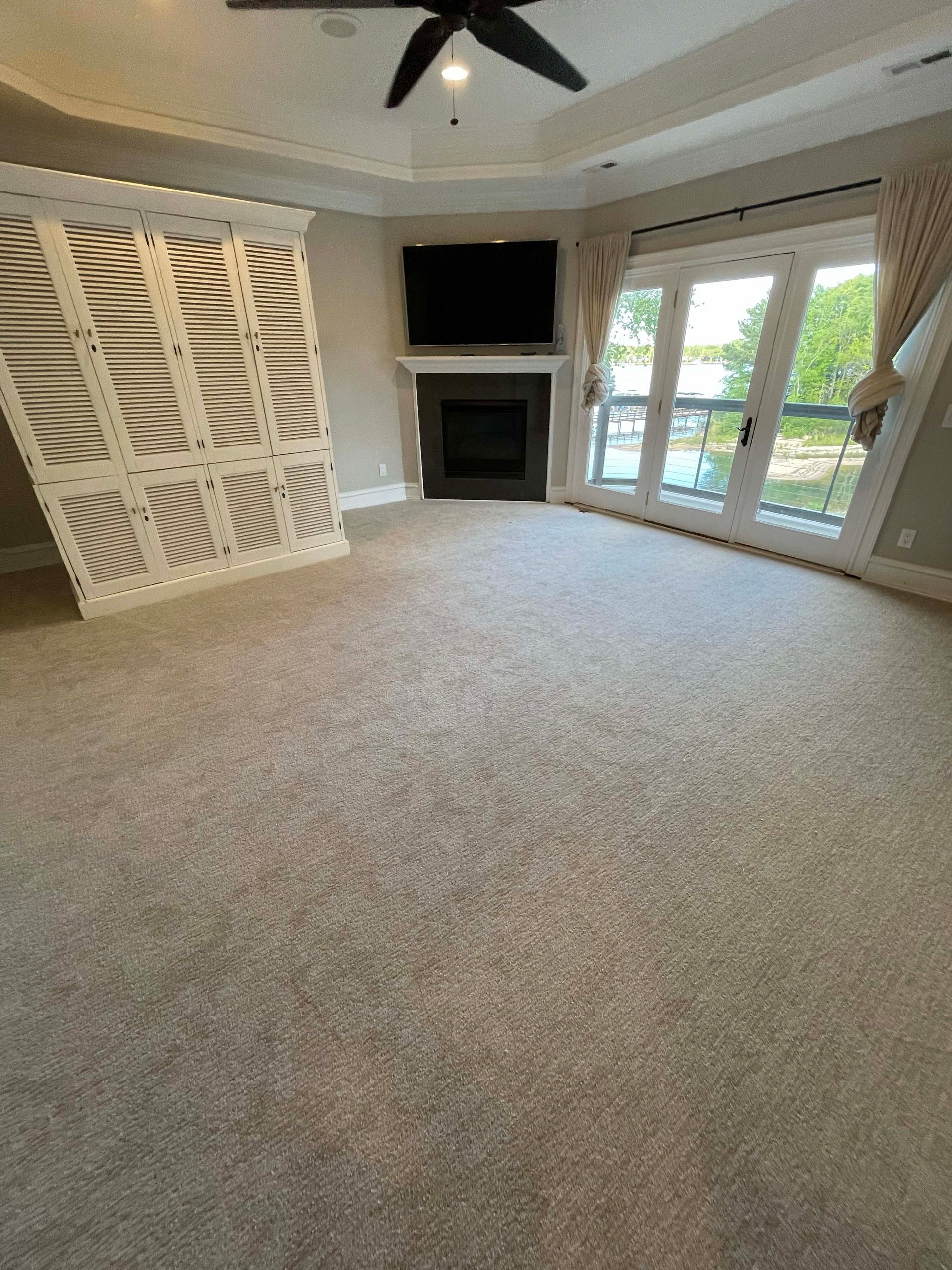 Empty carpeted living room with fireplace, TV, and French doors. A decorative wall panel is on the left.