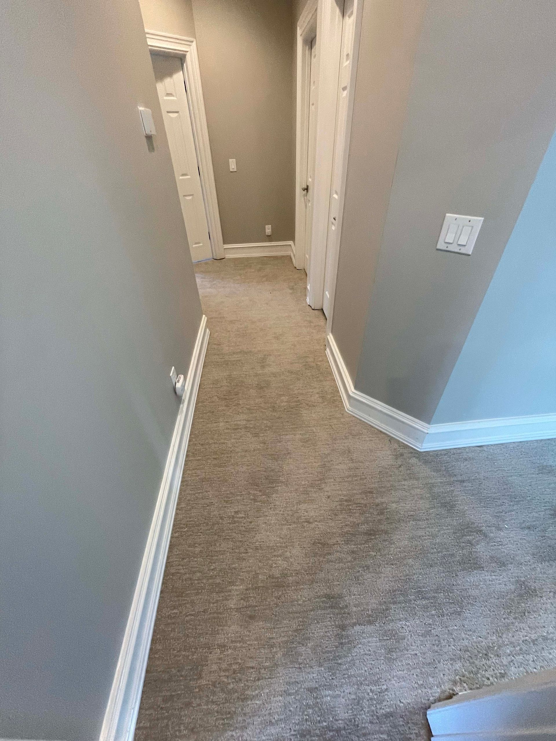 Narrow hallway with gray carpet, walls, and white trim; doors on either side.