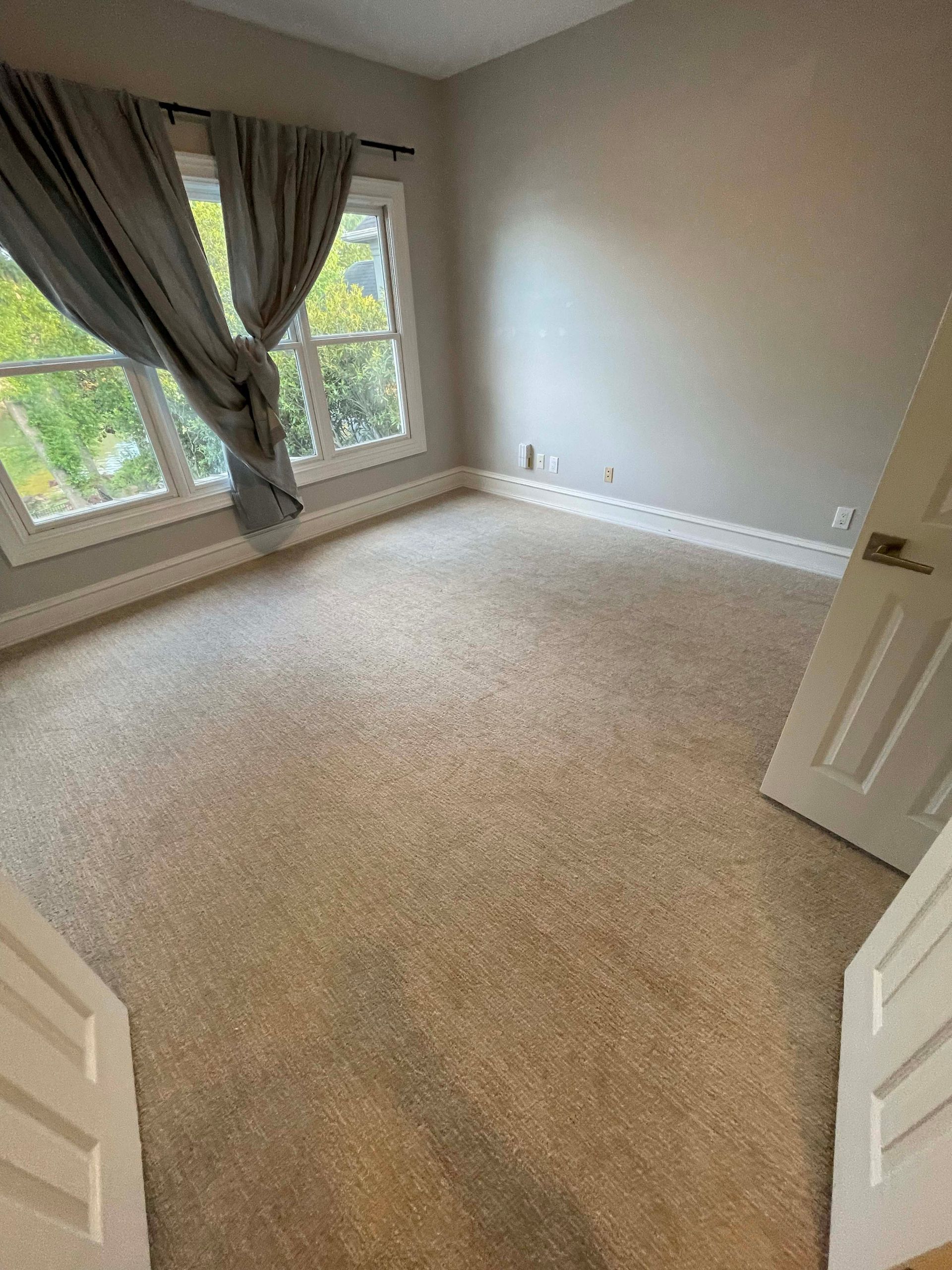 Empty room with beige carpet, window with gray curtain, and white trim.
