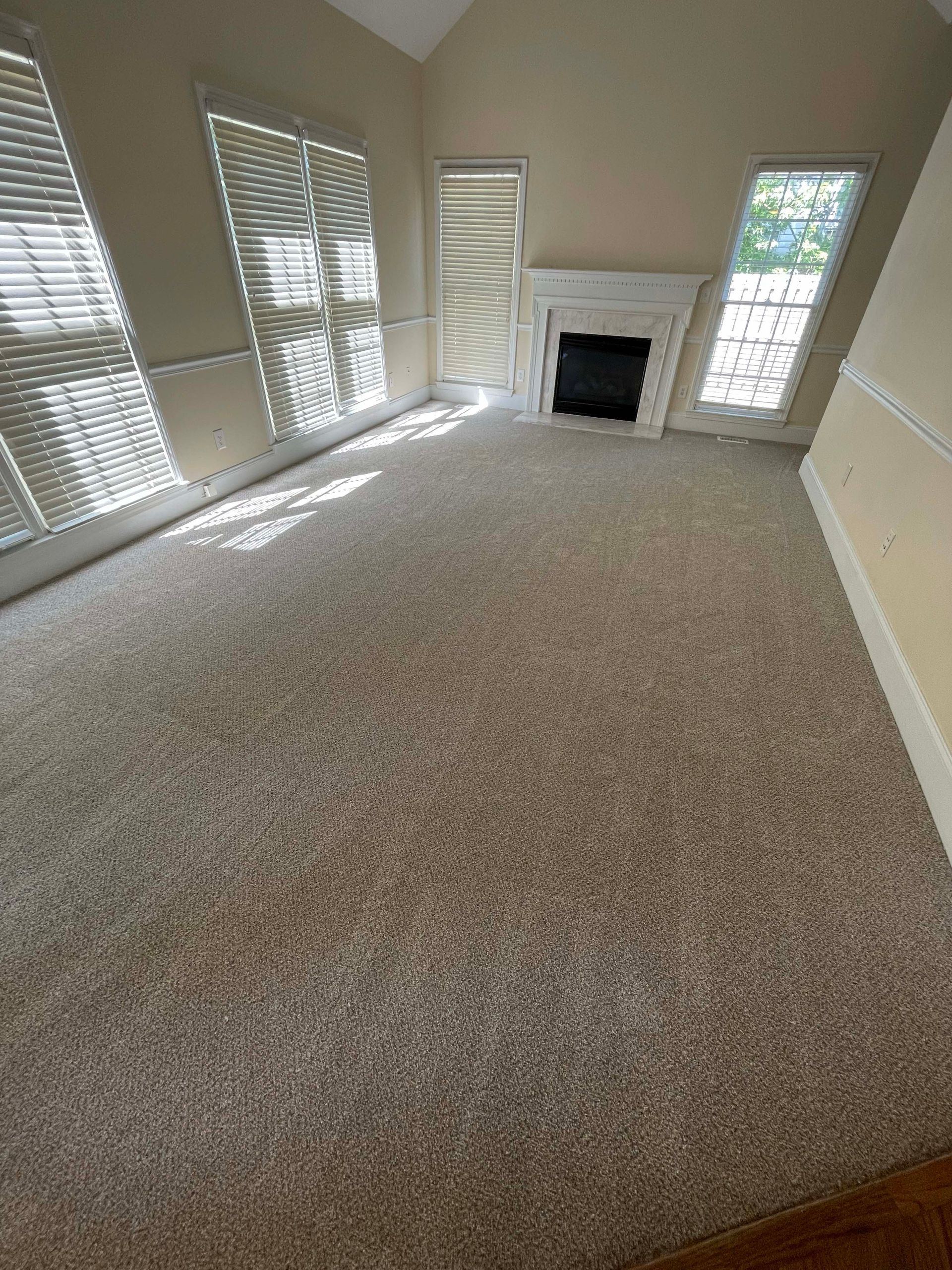 Living room with tan carpet, fireplace, and large windows with blinds.
