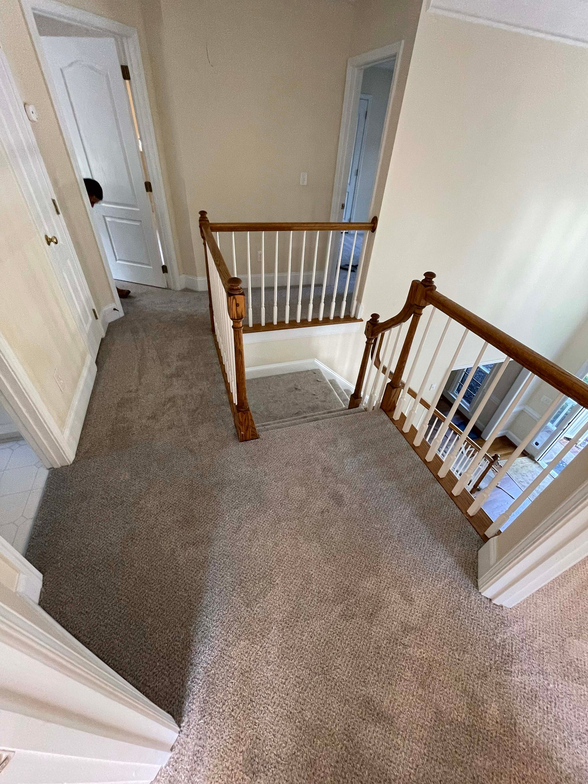 Staircase with brown wooden banisters and carpeted floors. A hallway with closed doors.