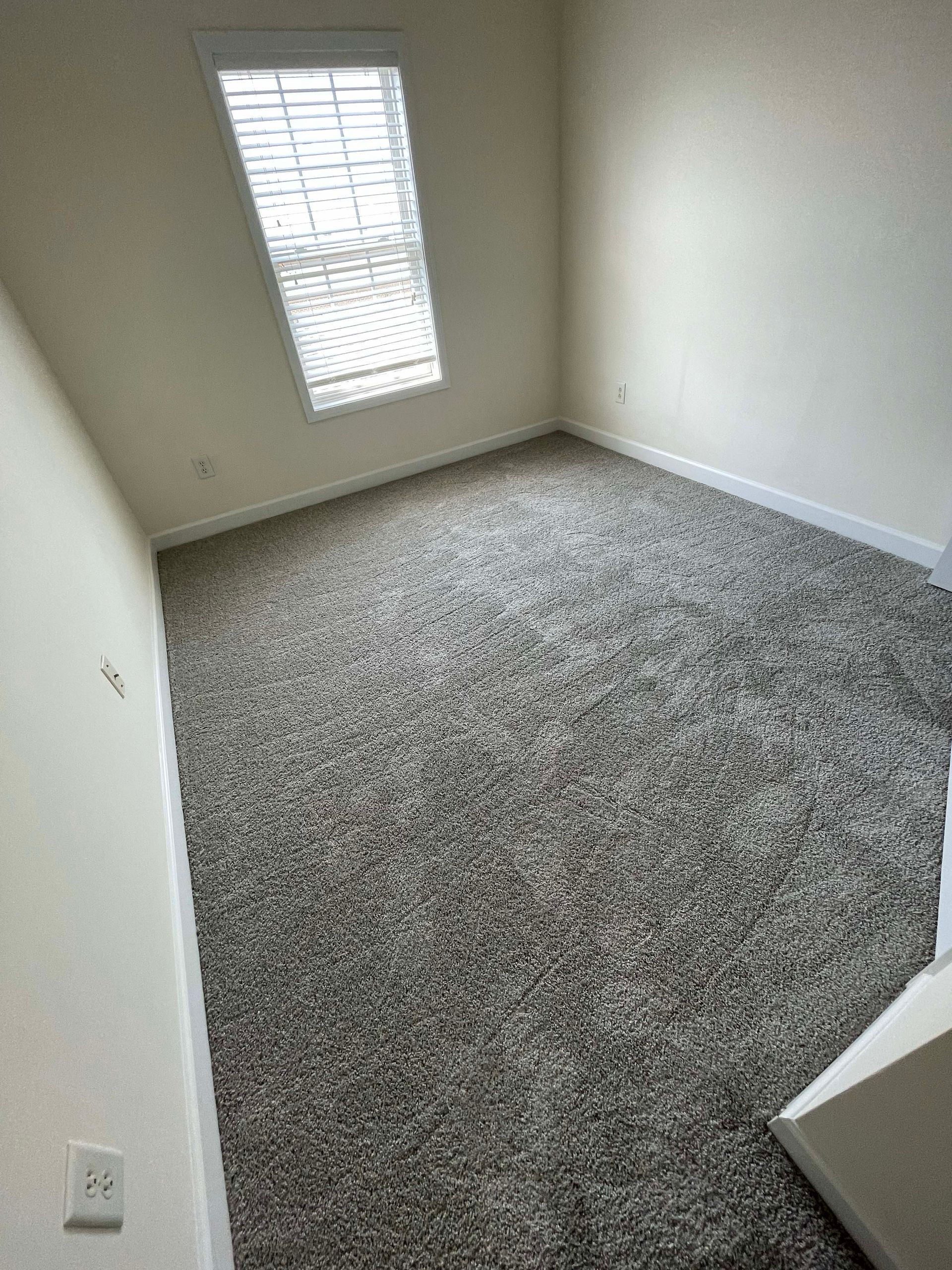 Empty room with gray speckled carpet, white walls, and a window with blinds.