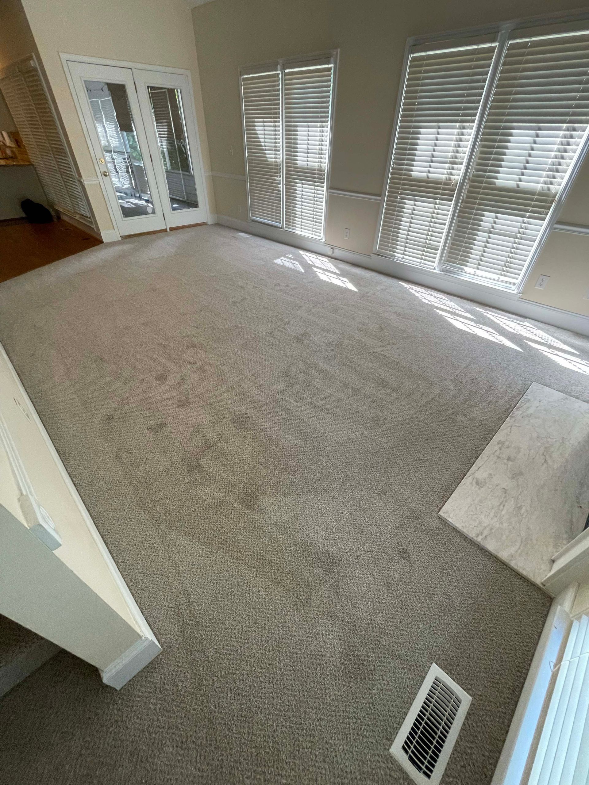 Carpeted room with a doorway, windows with blinds, and a vent.