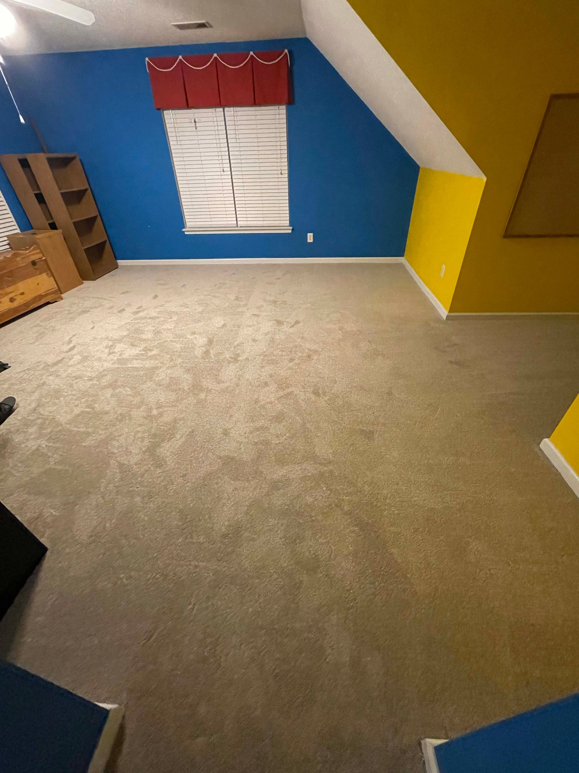 Empty room with blue and yellow walls, beige carpet, and a window with blinds.