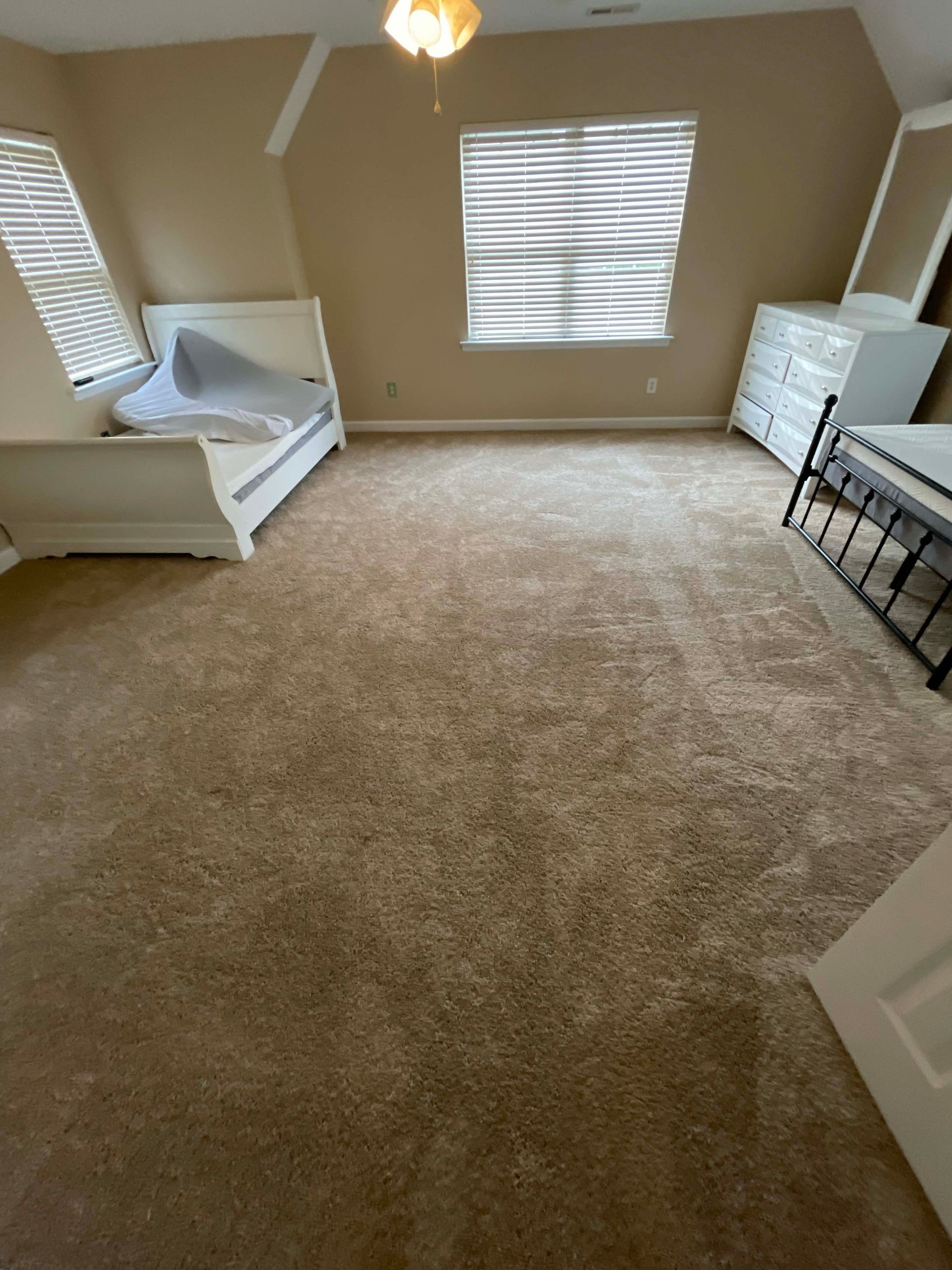 Bedroom with carpet, two beds, white dresser, and window with blinds. Beige walls and ceiling fan.