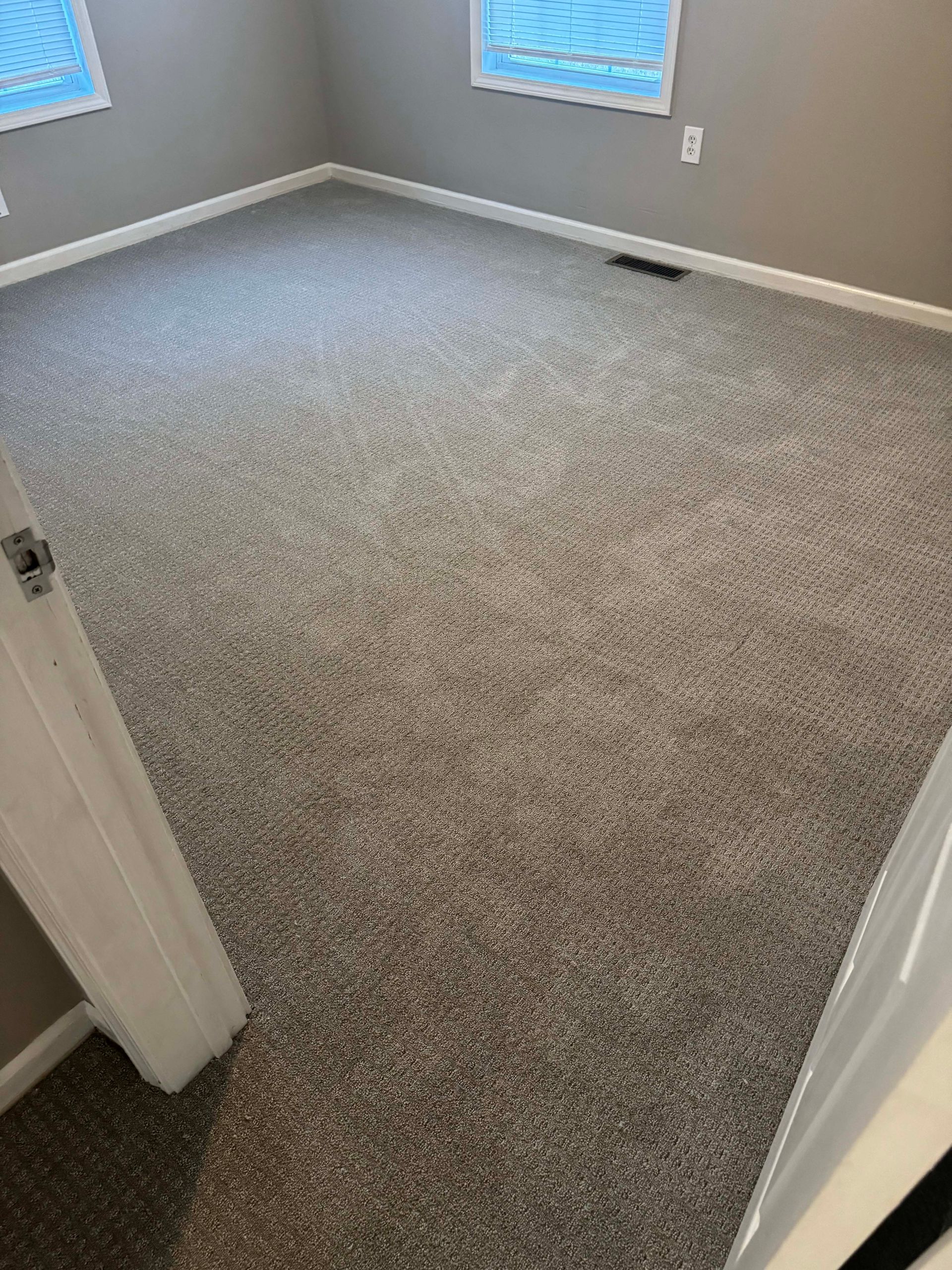 Empty room with gray carpeting, white trim, and gray walls. Two windows are visible.