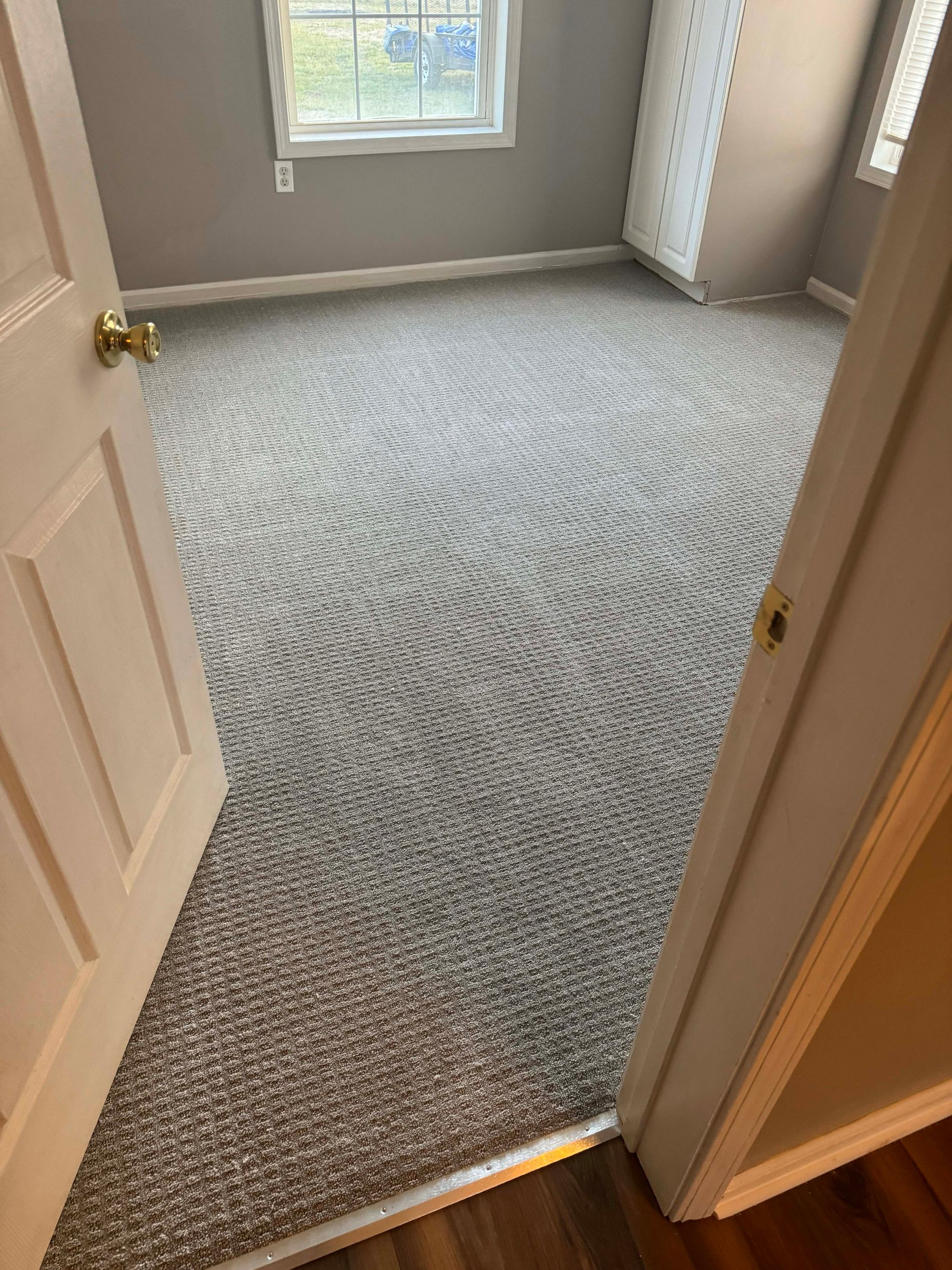 Bedroom with gray patterned carpet, a window, and an open doorway.