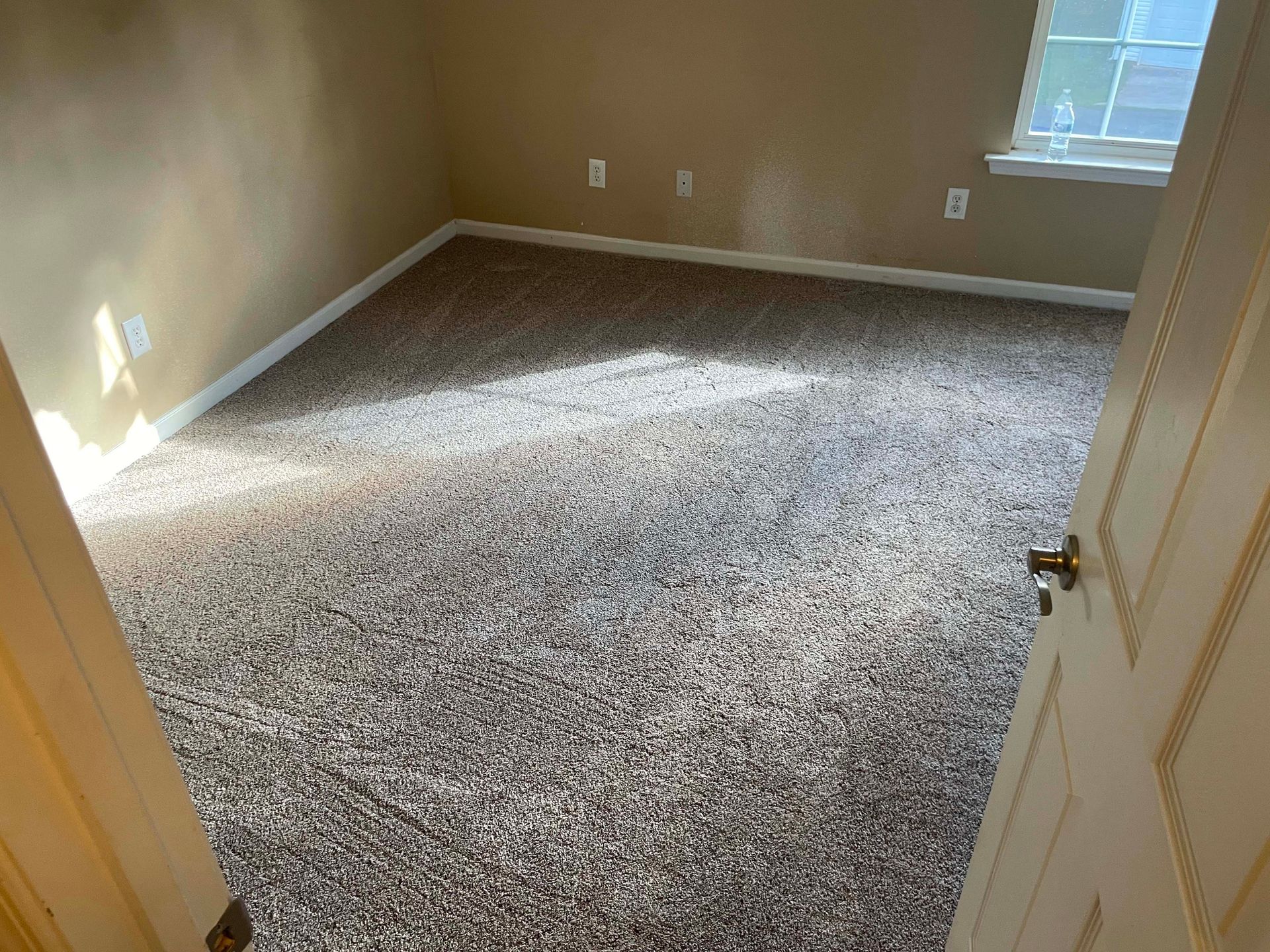 Empty room with new speckled carpet and beige walls. Doorway on the right, window on the right.