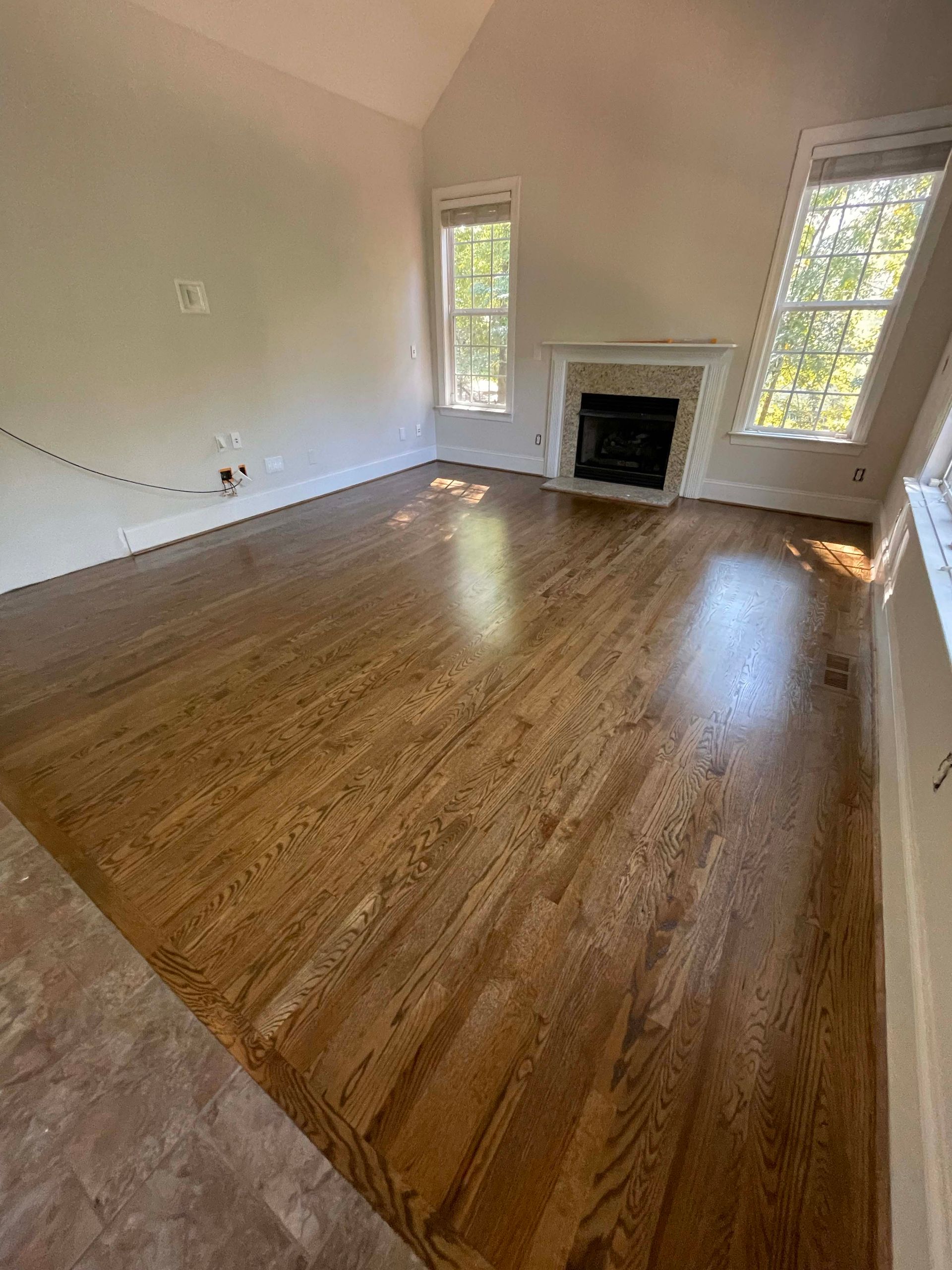 Hardwood floor in a living room with fireplace and two windows.