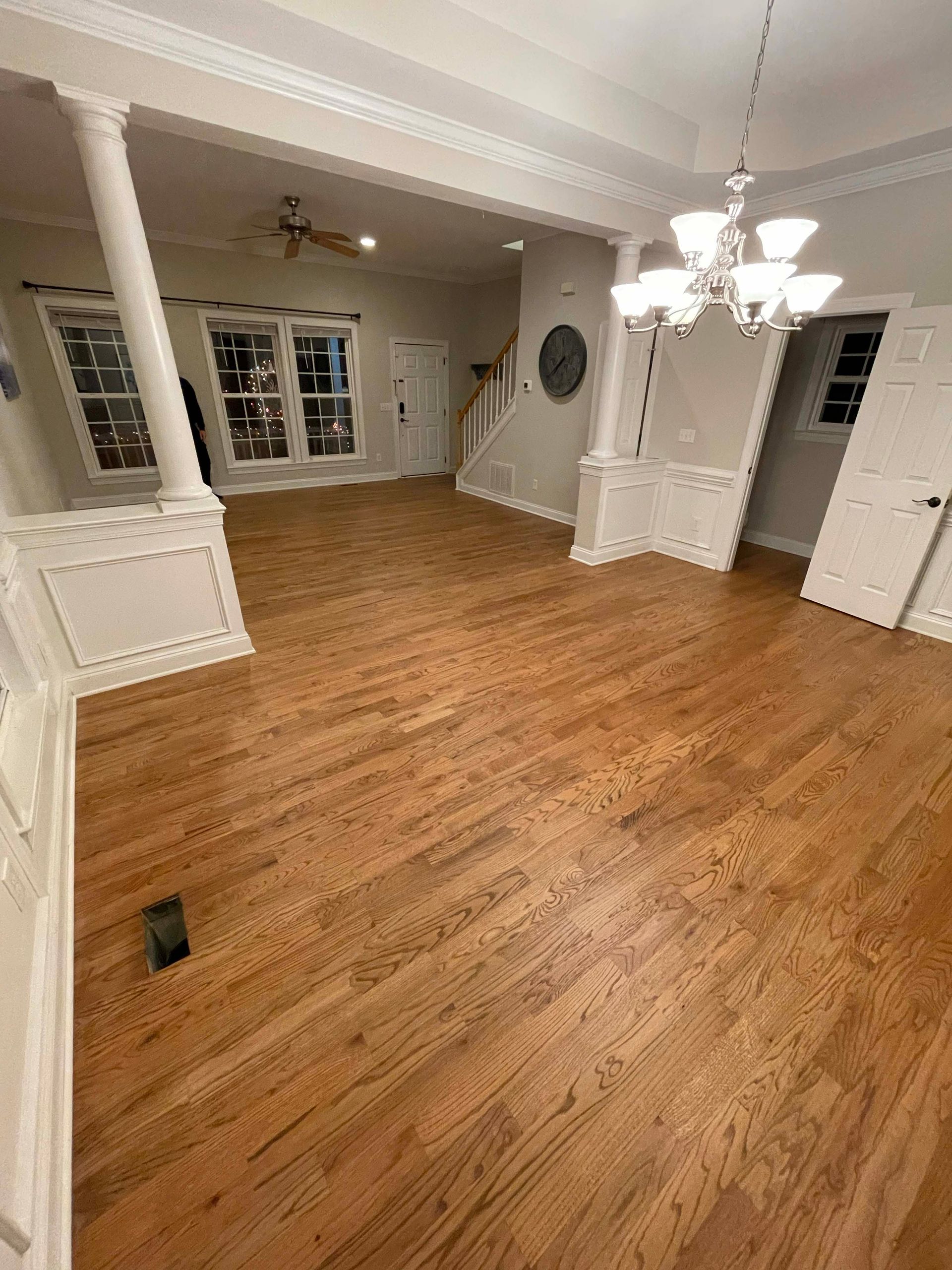 Wooden floors in a bright, empty room with white pillars, crown molding, and a chandelier.