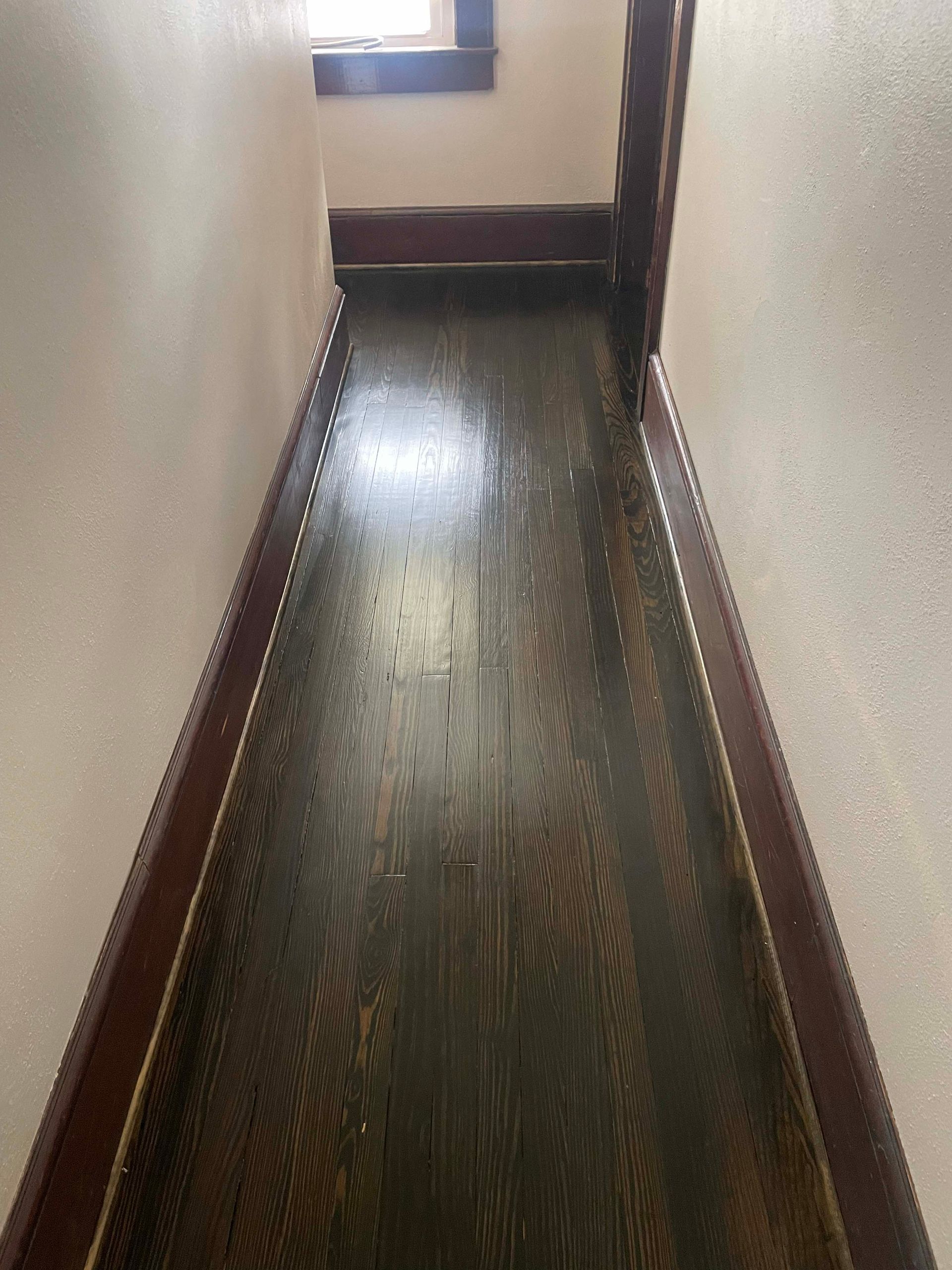 Narrow hallway with dark wood floor and trim, pale pink walls, and a small window at top.