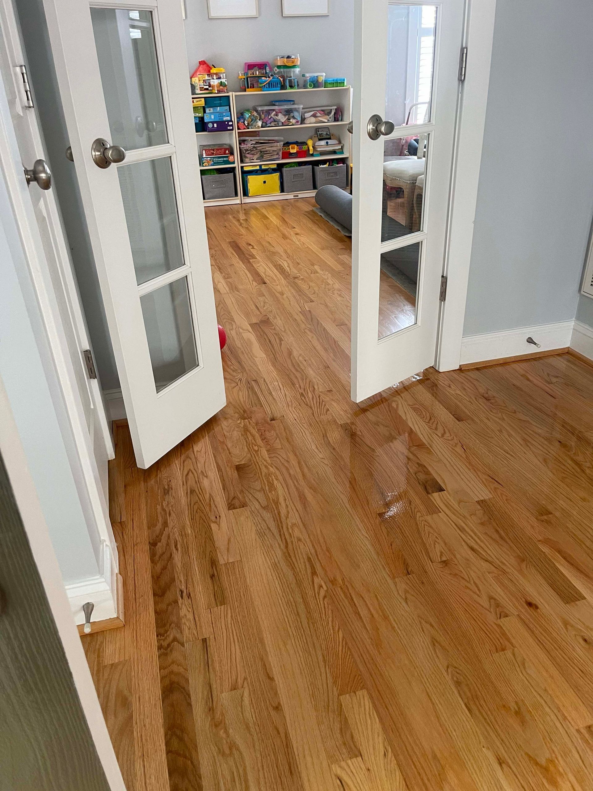 Hardwood floors lead to a room with toys and storage shelves, seen through open white French doors.