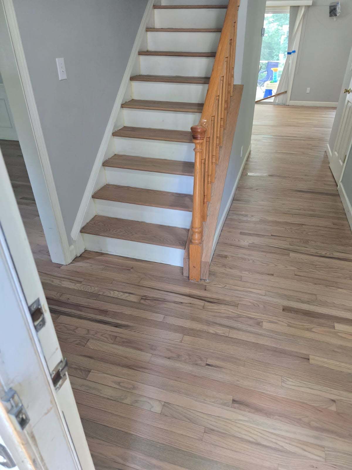 Hardwood flooring and staircase in a home. The staircase has a wooden handrail and carpeted steps.