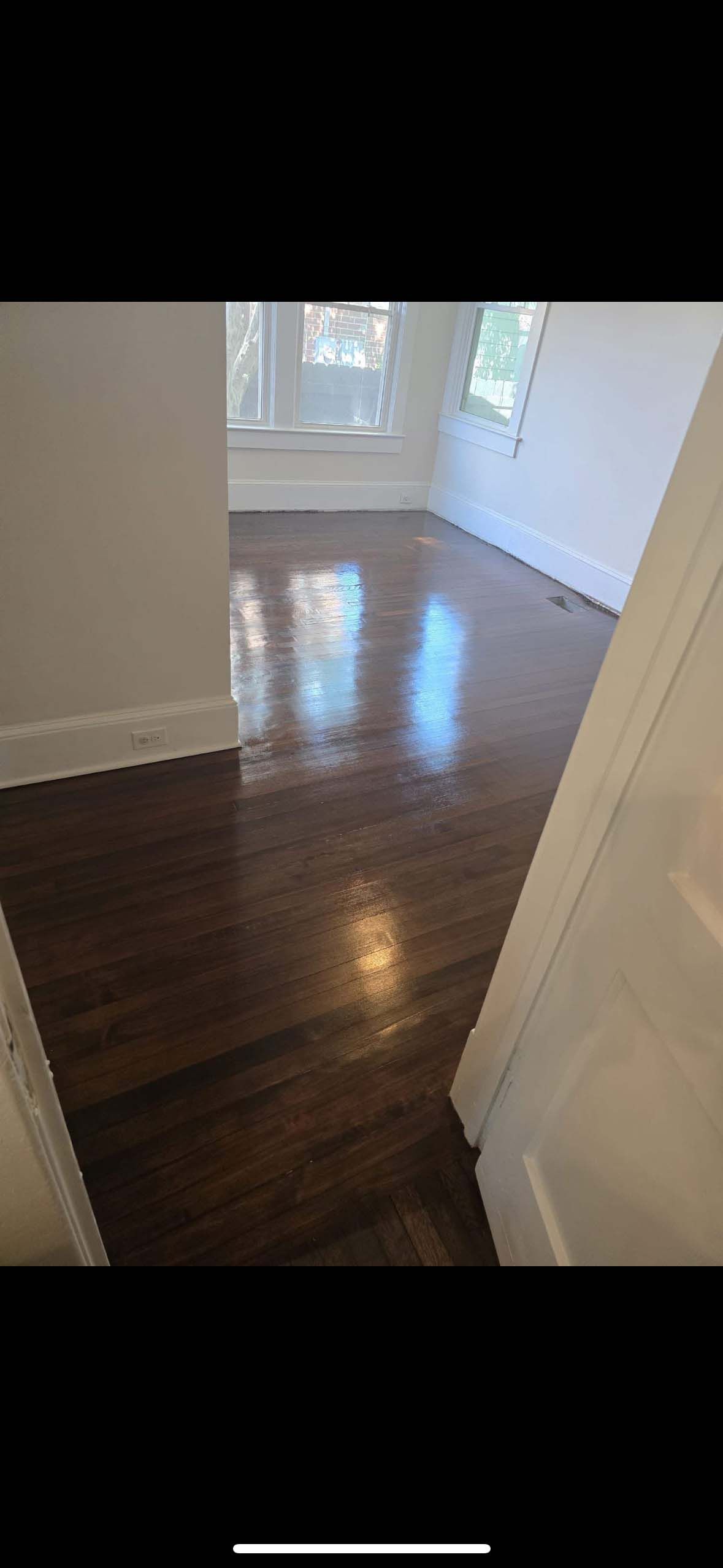 Dark hardwood floor in a room, with sunlight reflecting off it. White trim and walls.