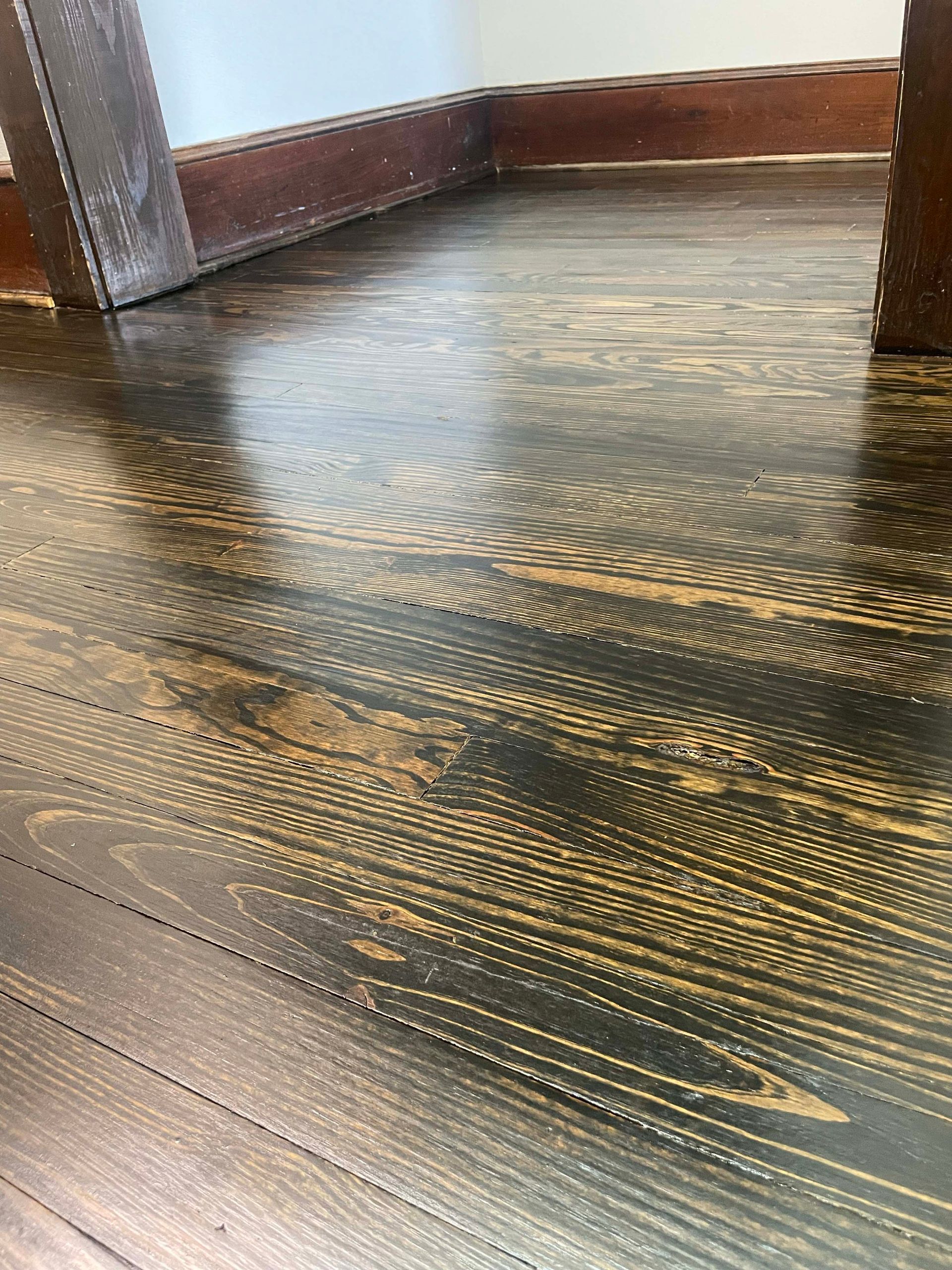Close-up of a dark stained wooden floor with visible grain and a glossy finish.