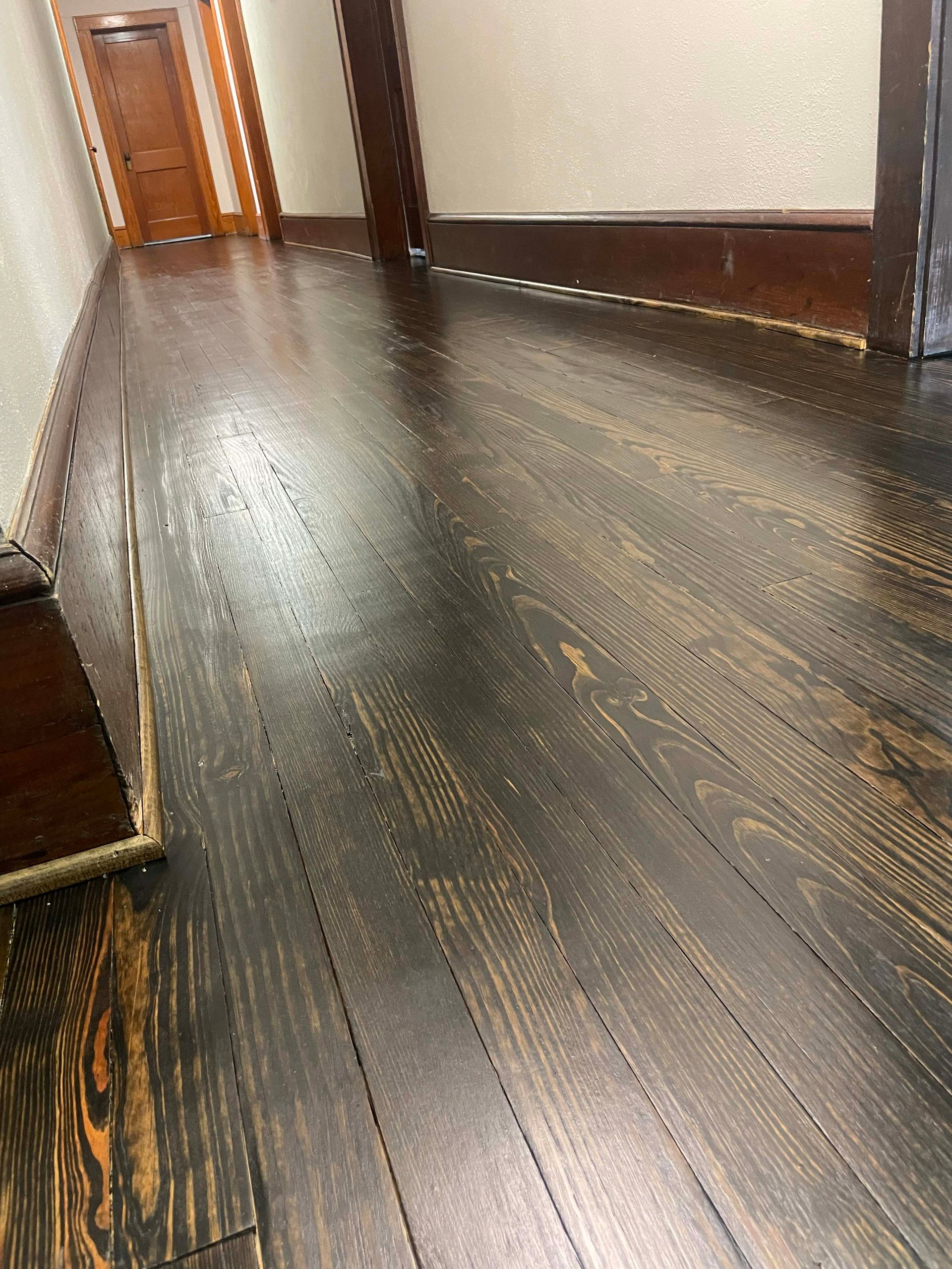 Dark stained wood floor in a hallway. Brown trim, doorway, and baseboards.