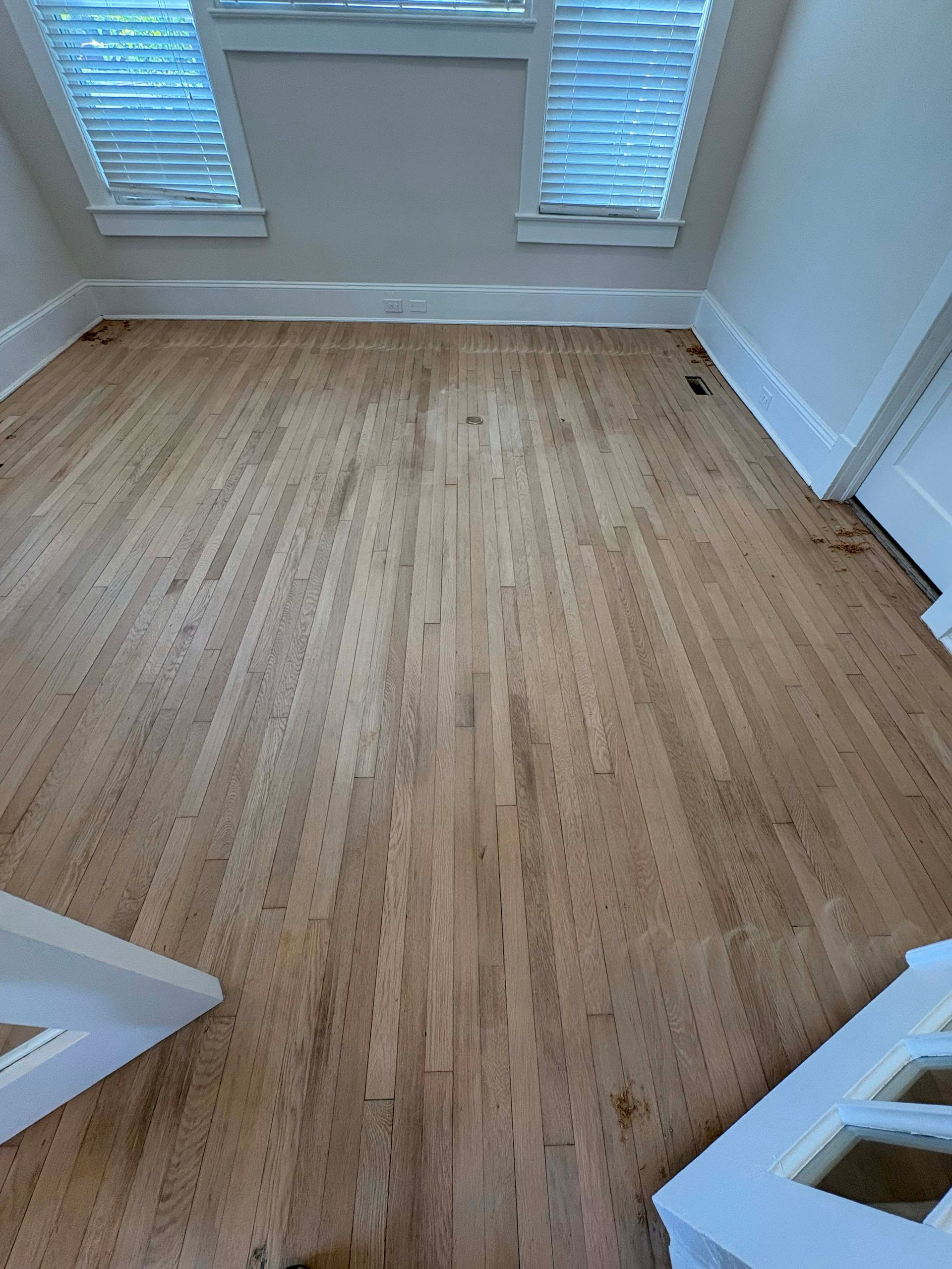 Hardwood floor in room with windows and white trim.