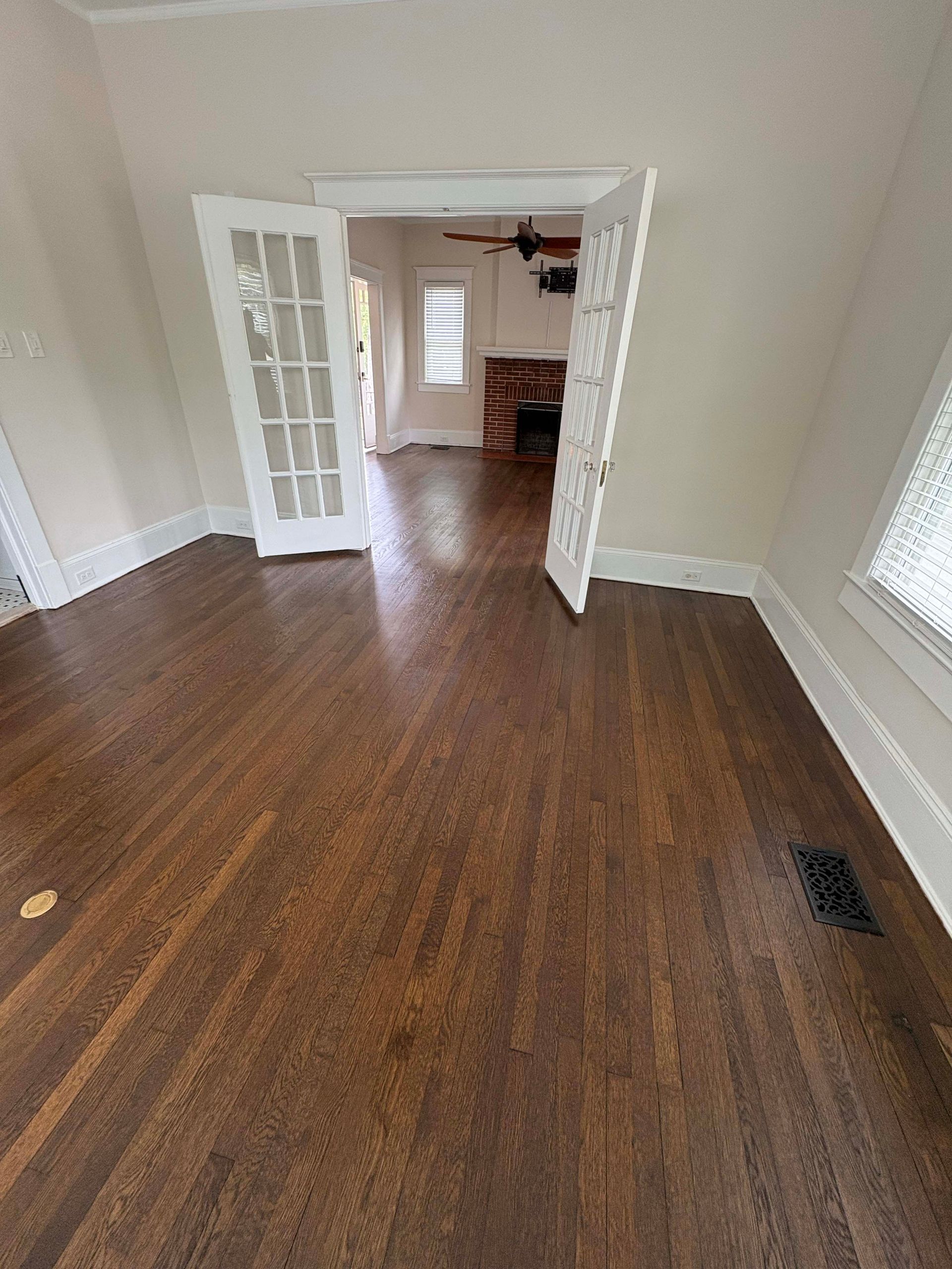 Hardwood floor, French doors open to a room with a fireplace and windows.