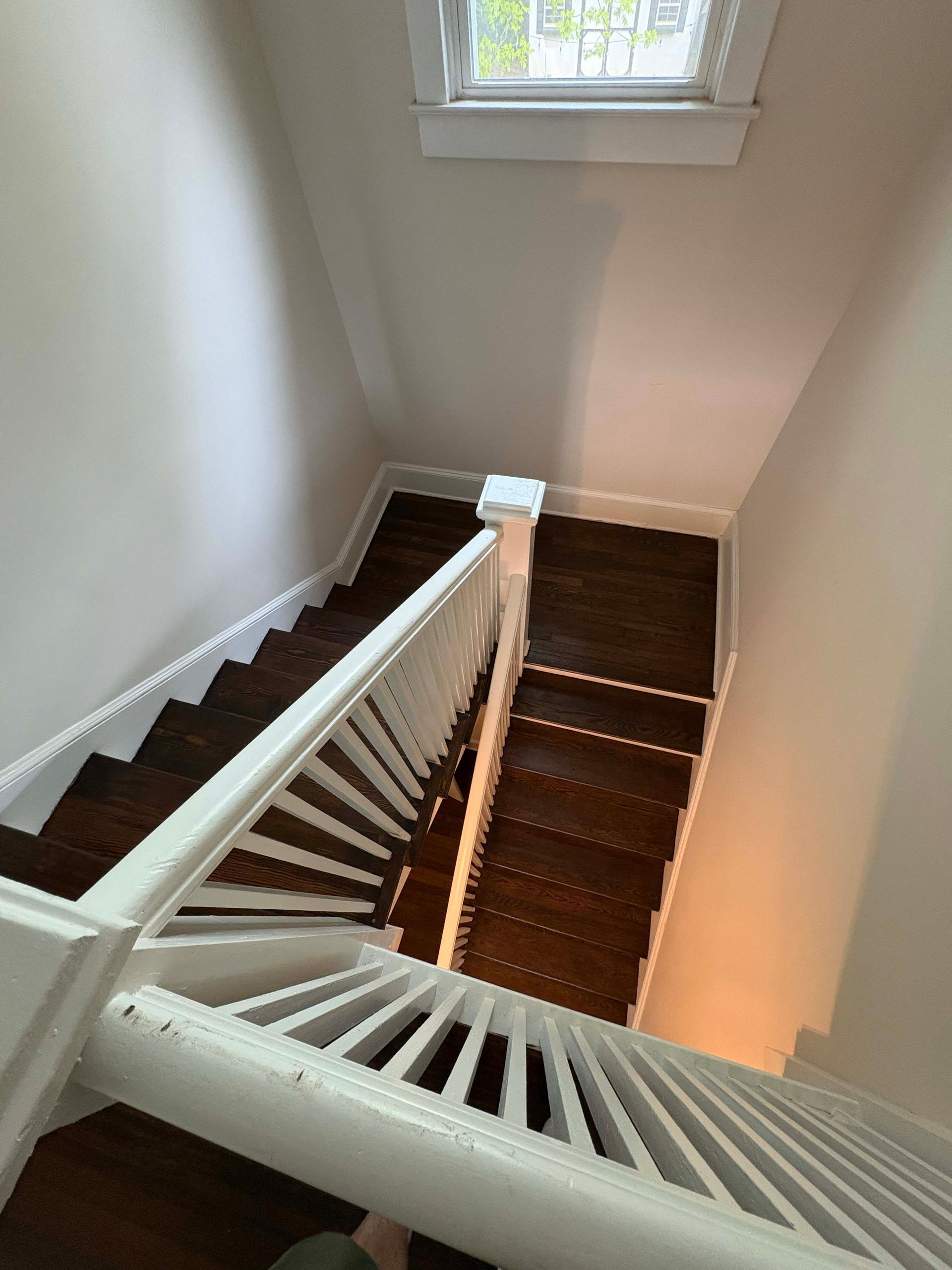 Staircase with dark wood steps and white railing, viewed from above. Window at top.
