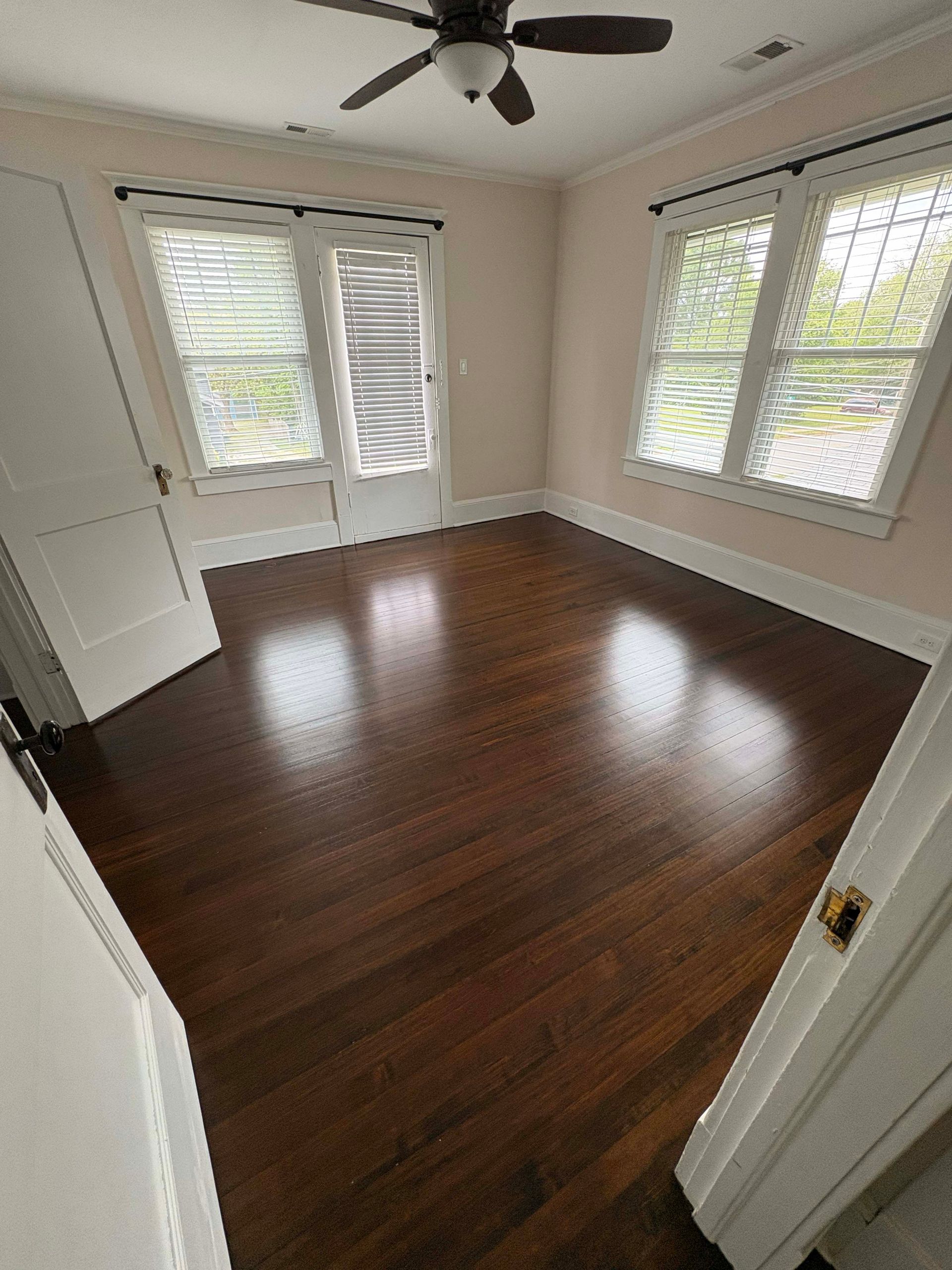Empty bedroom with dark hardwood floors, two windows with white shutters, and a ceiling fan.