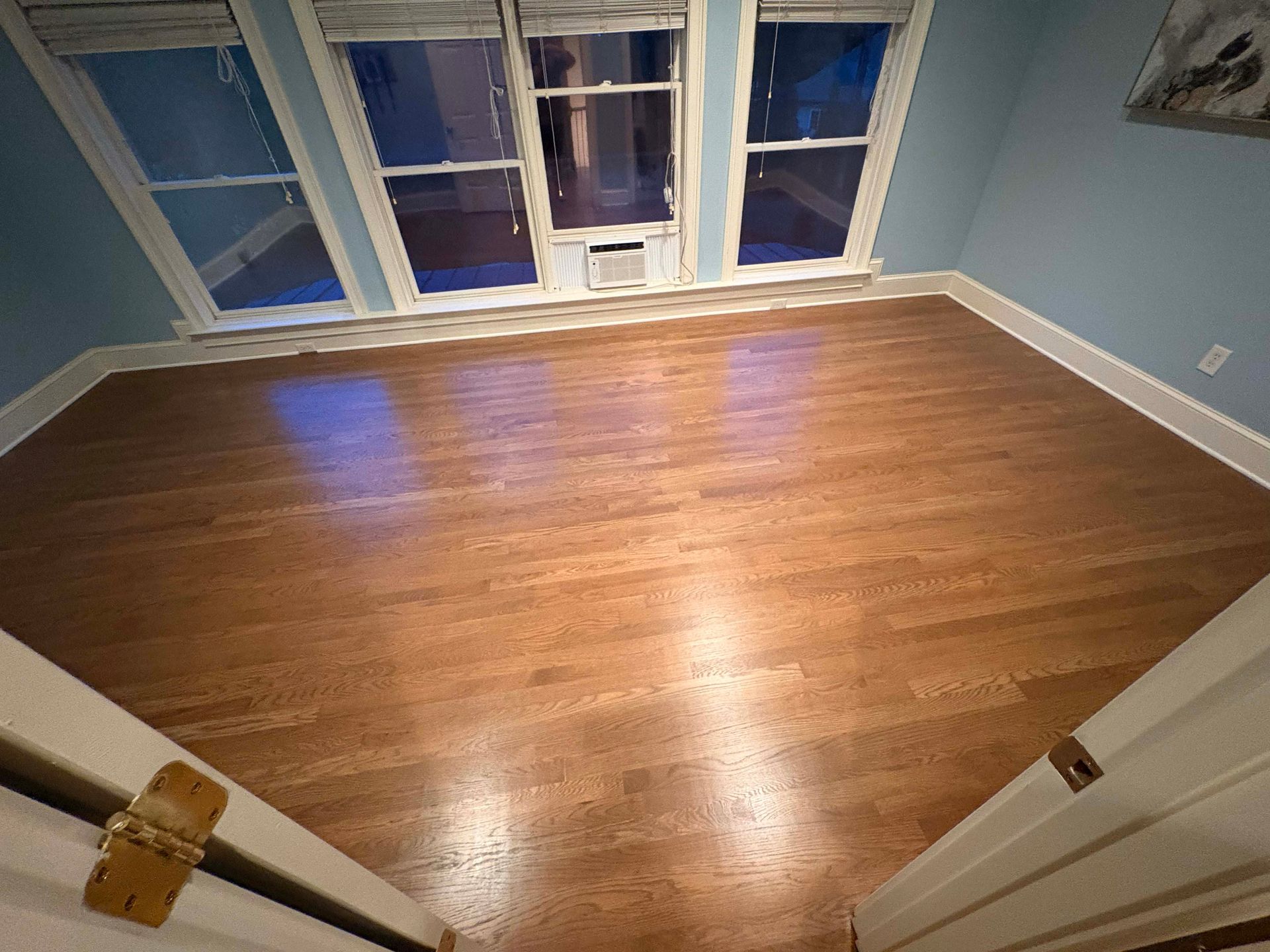Empty room with hardwood floors, blue walls, and windows.