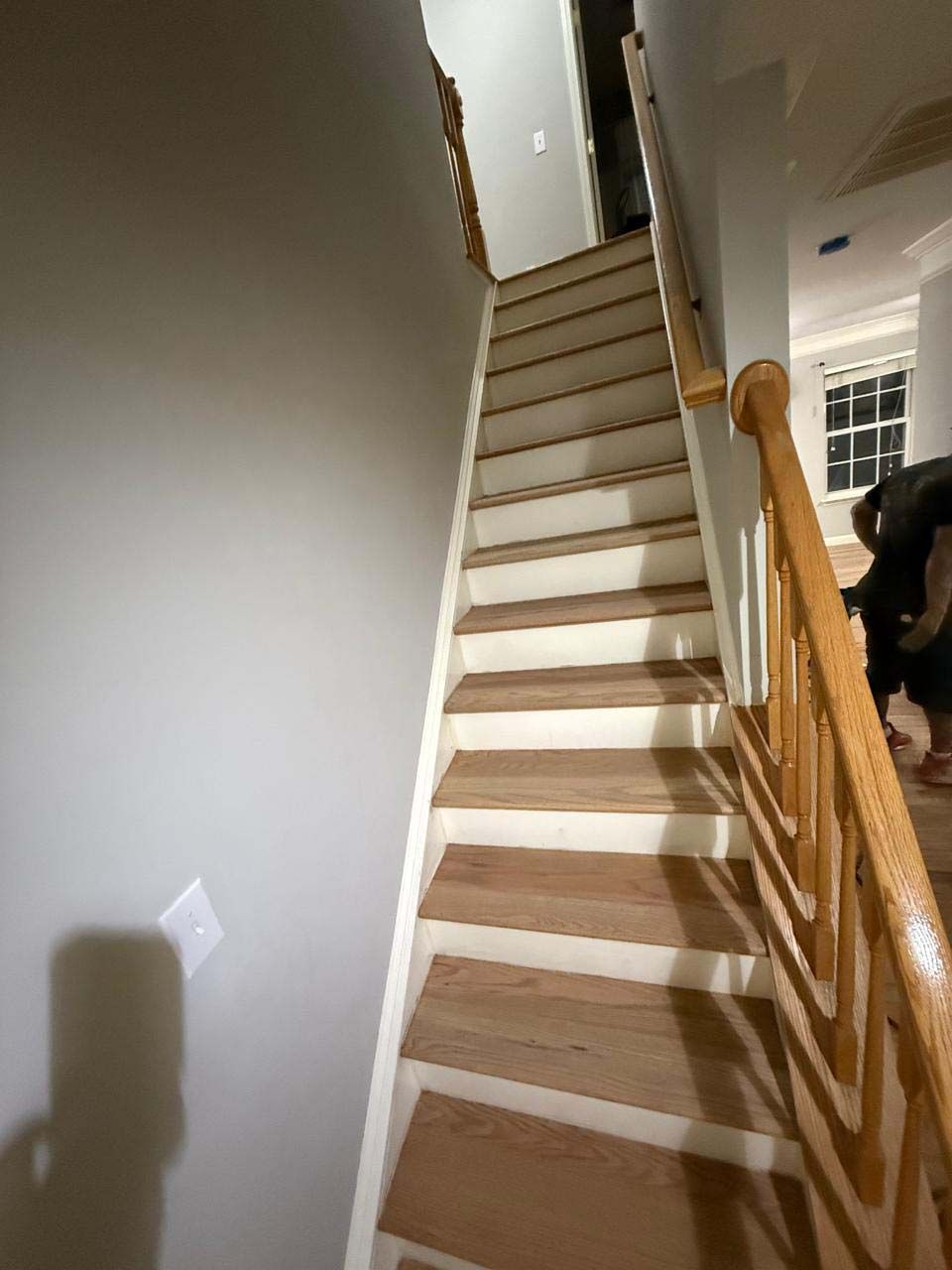 Wooden staircase with white risers, wood railing, and light gray walls.