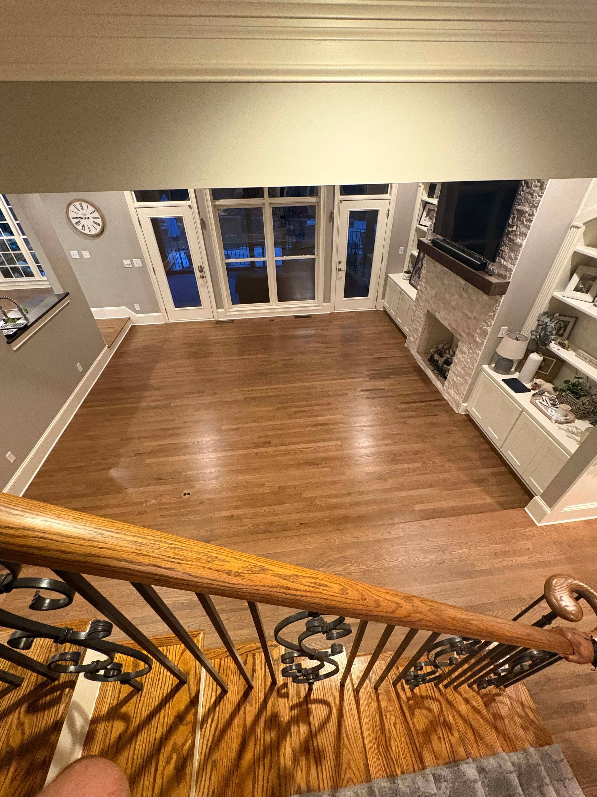 Looking down a staircase into a living room with wooden floors, French doors, fireplace, and built-in shelves.