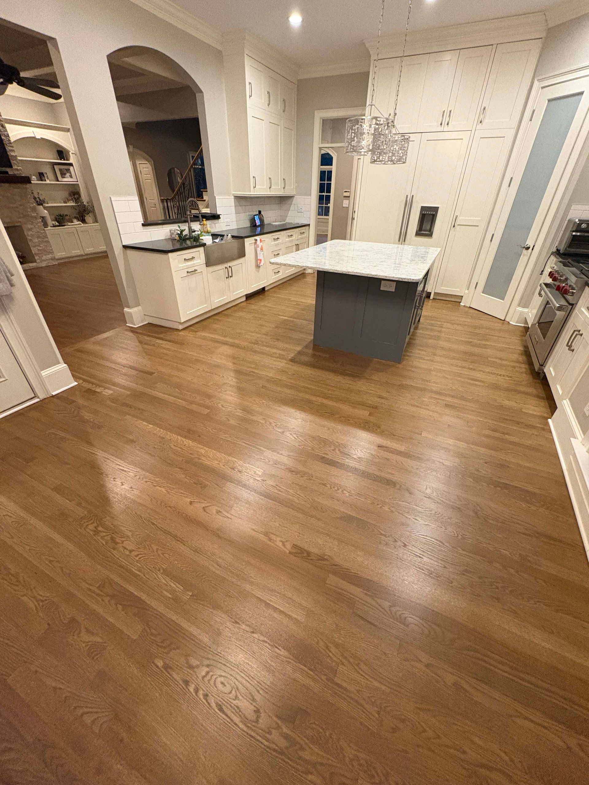 Hardwood floor in a kitchen with white cabinets, island, and appliances.