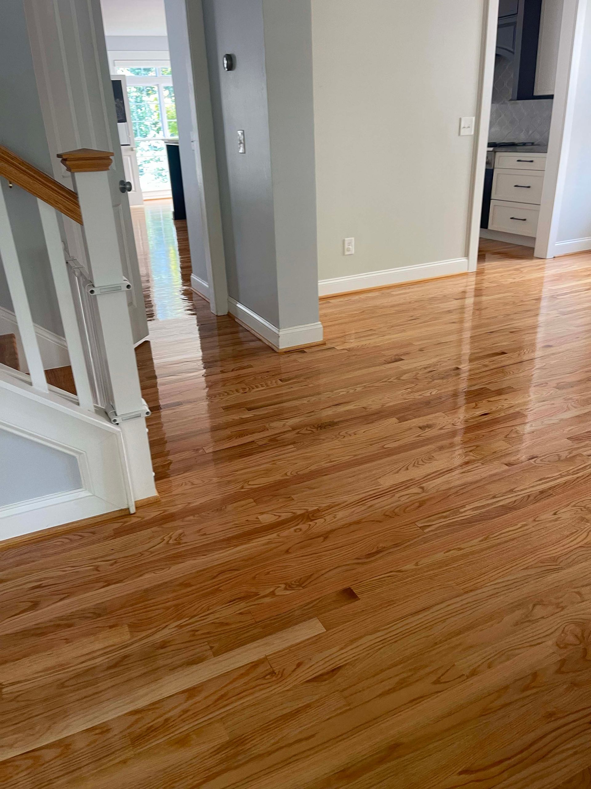 Hardwood floor in home with a staircase on the left and a doorway to kitchen on the right.