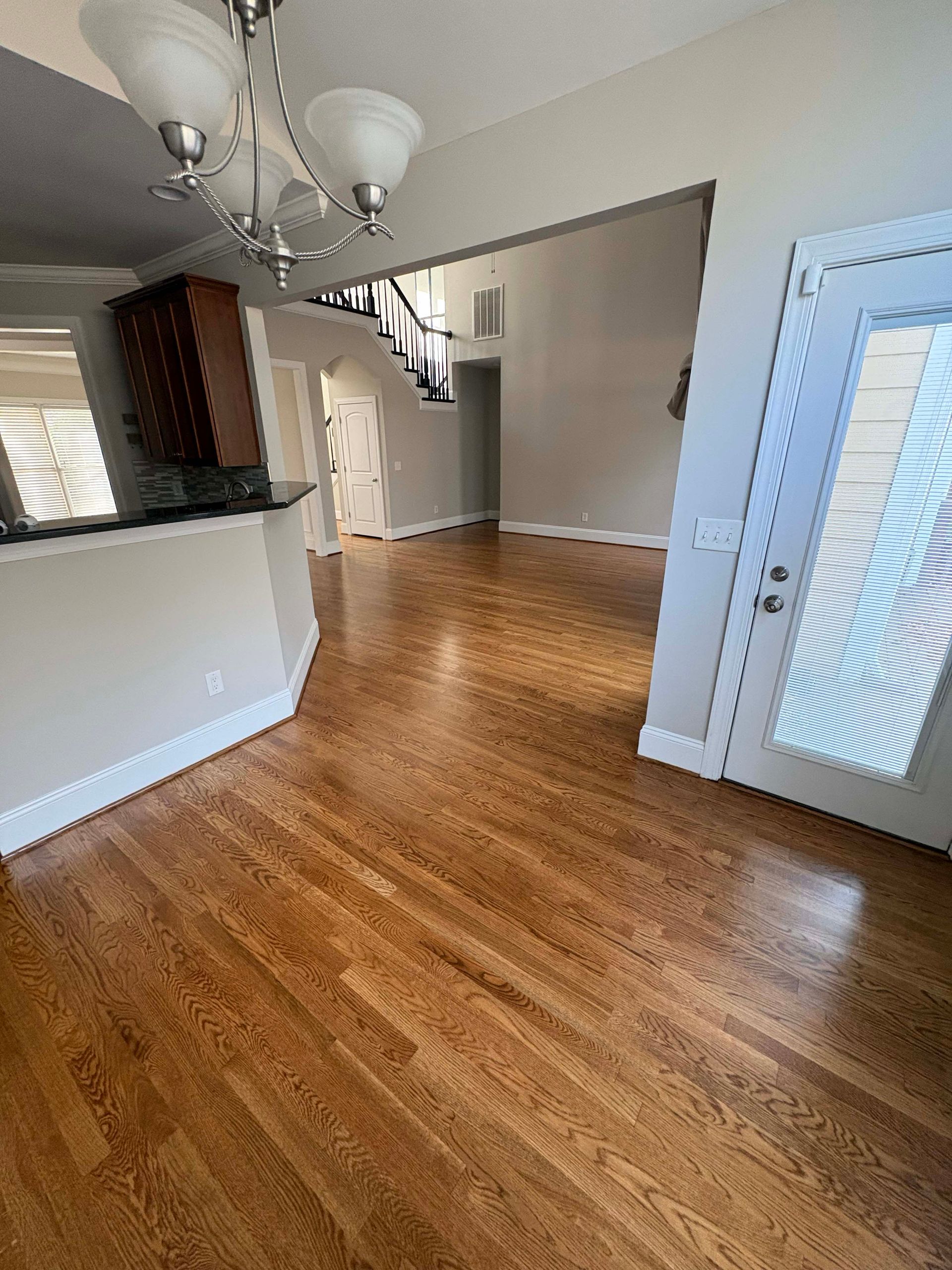Hardwood floor in an empty room, leading to a staircase and front door. Light beige walls.