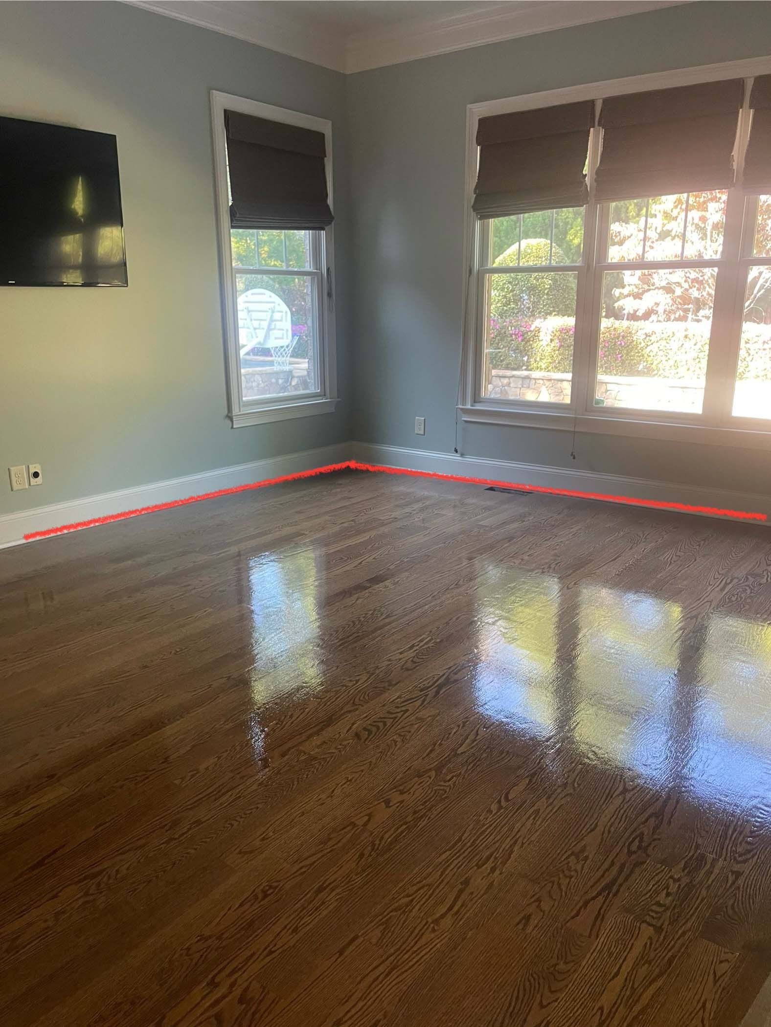Room with shiny wooden floor, blue walls, two windows with blinds, and a TV on the wall.