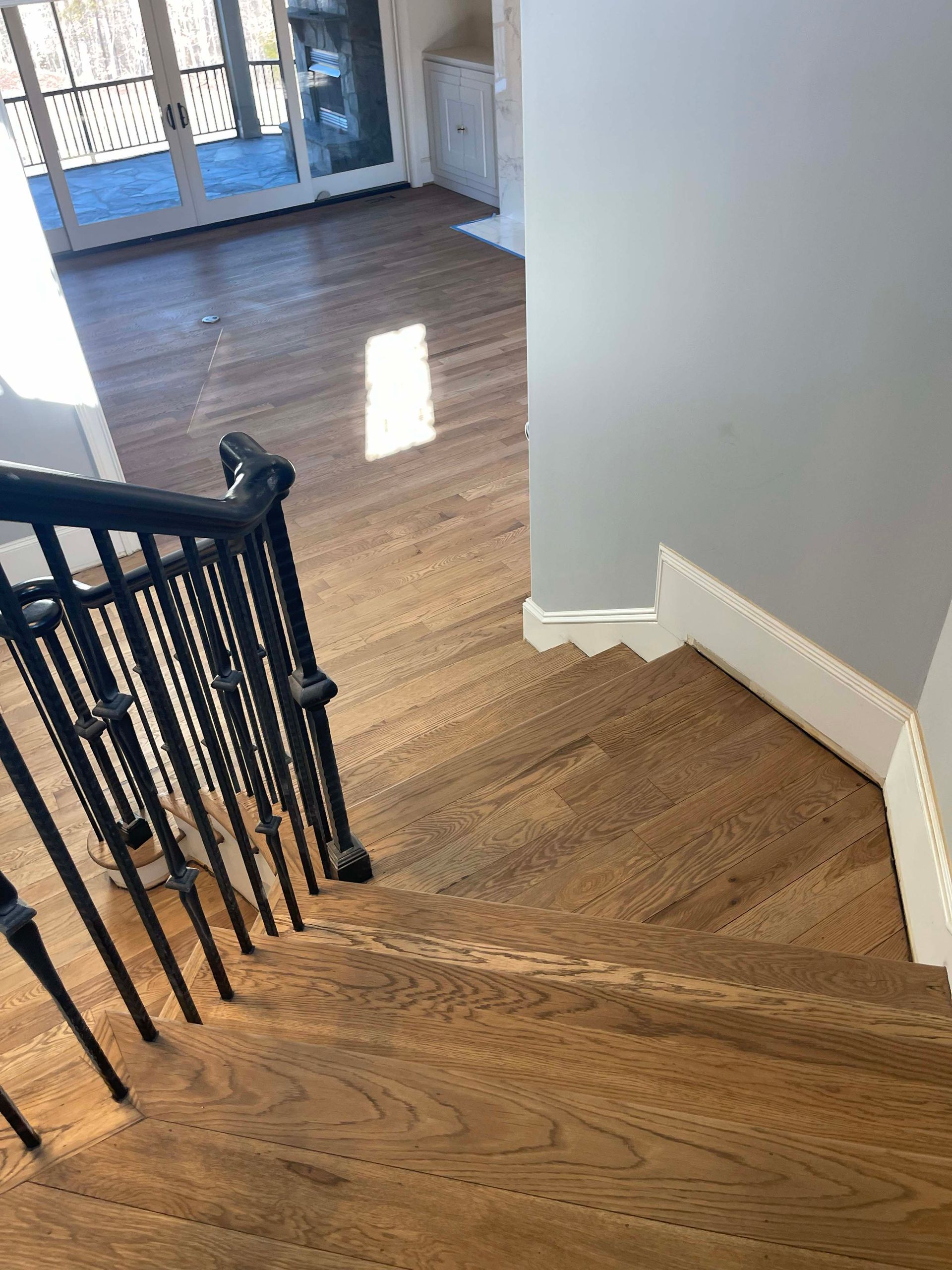 Wooden staircase with black railing leads down to a light-filled room with hardwood floors.