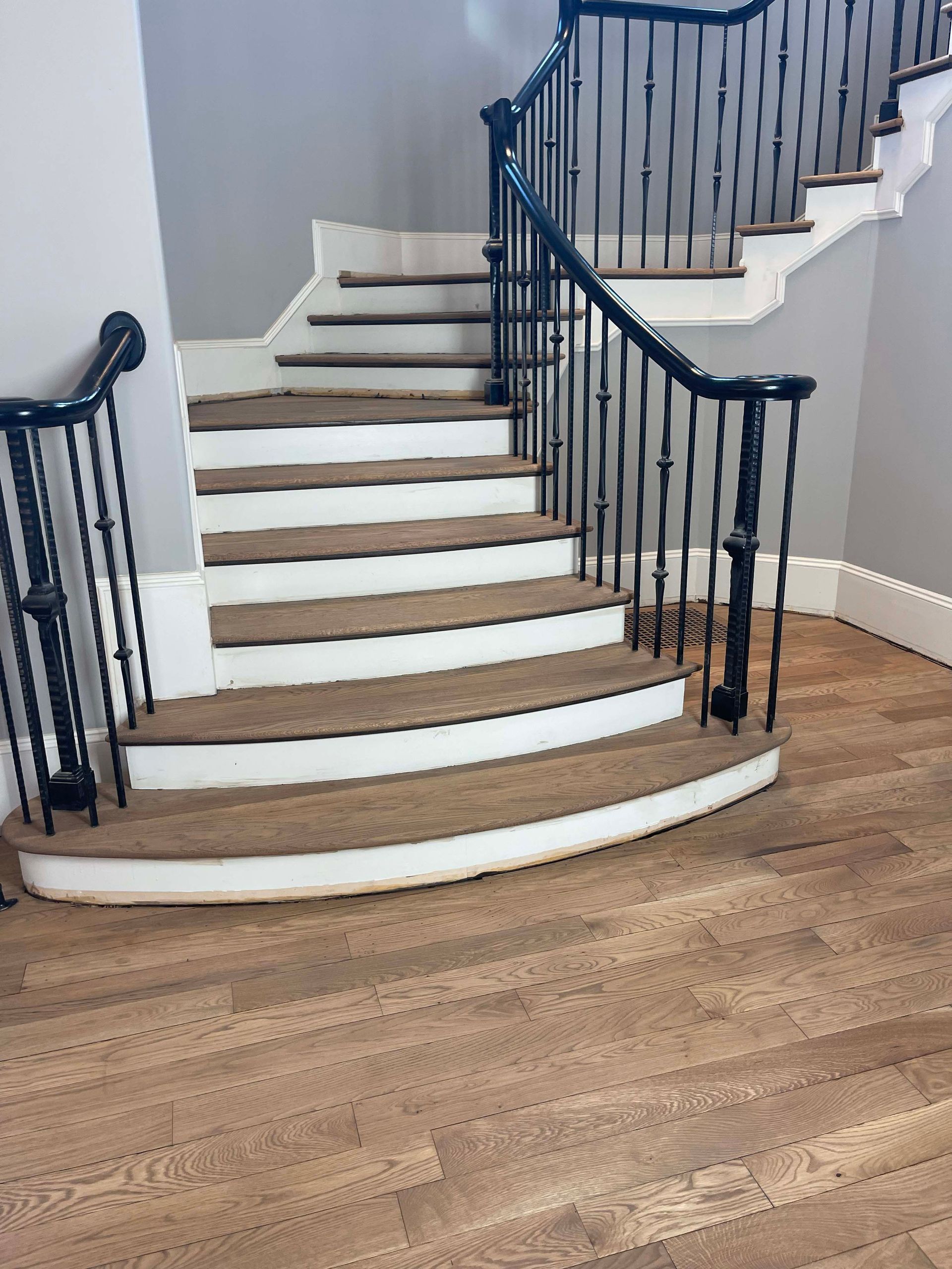 Staircase with brown carpet treads, white risers, and black iron railing in a home.