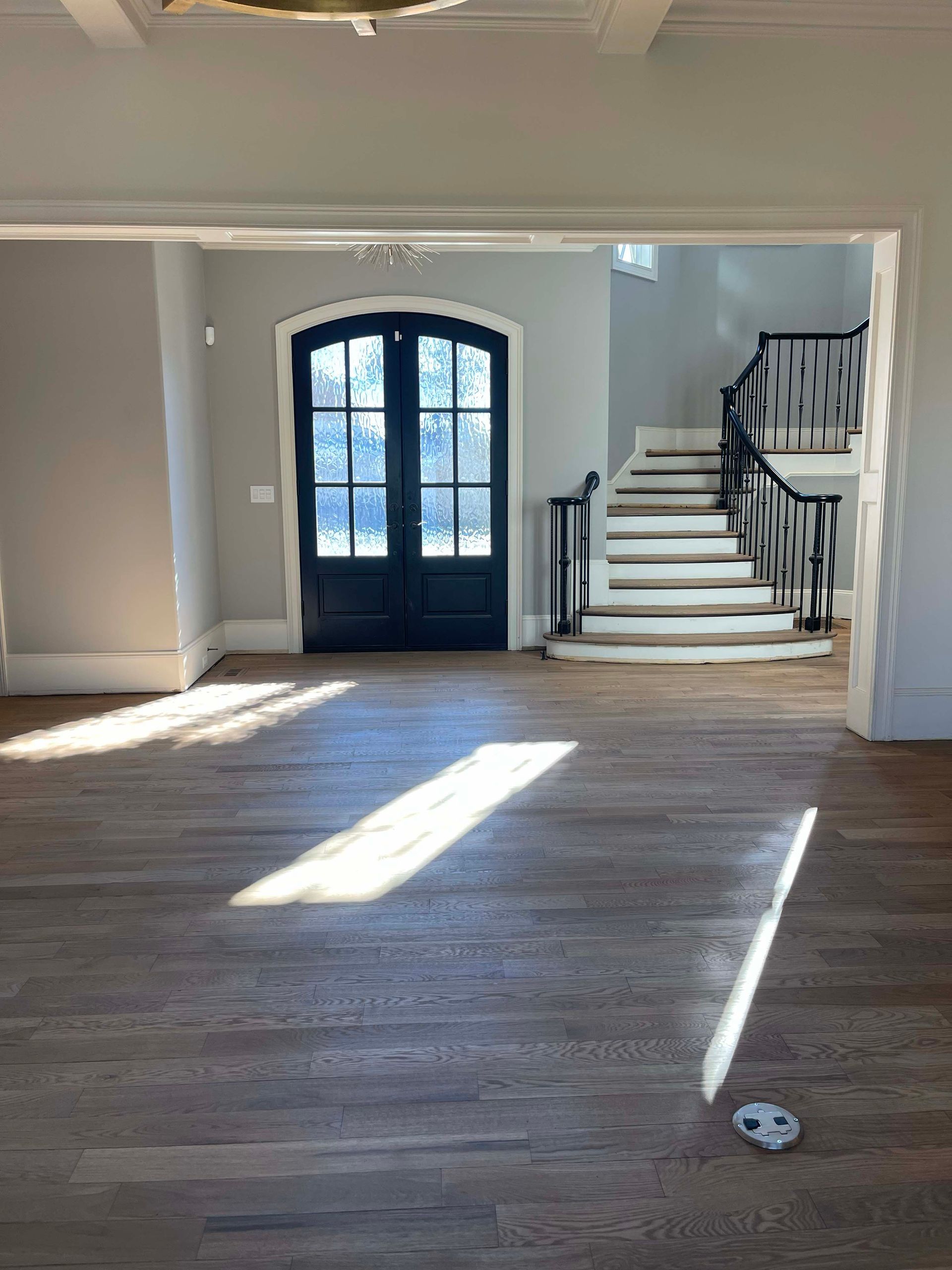 Interior of a home with hardwood floors, front door, and a staircase. Sunlight streams across the floor.