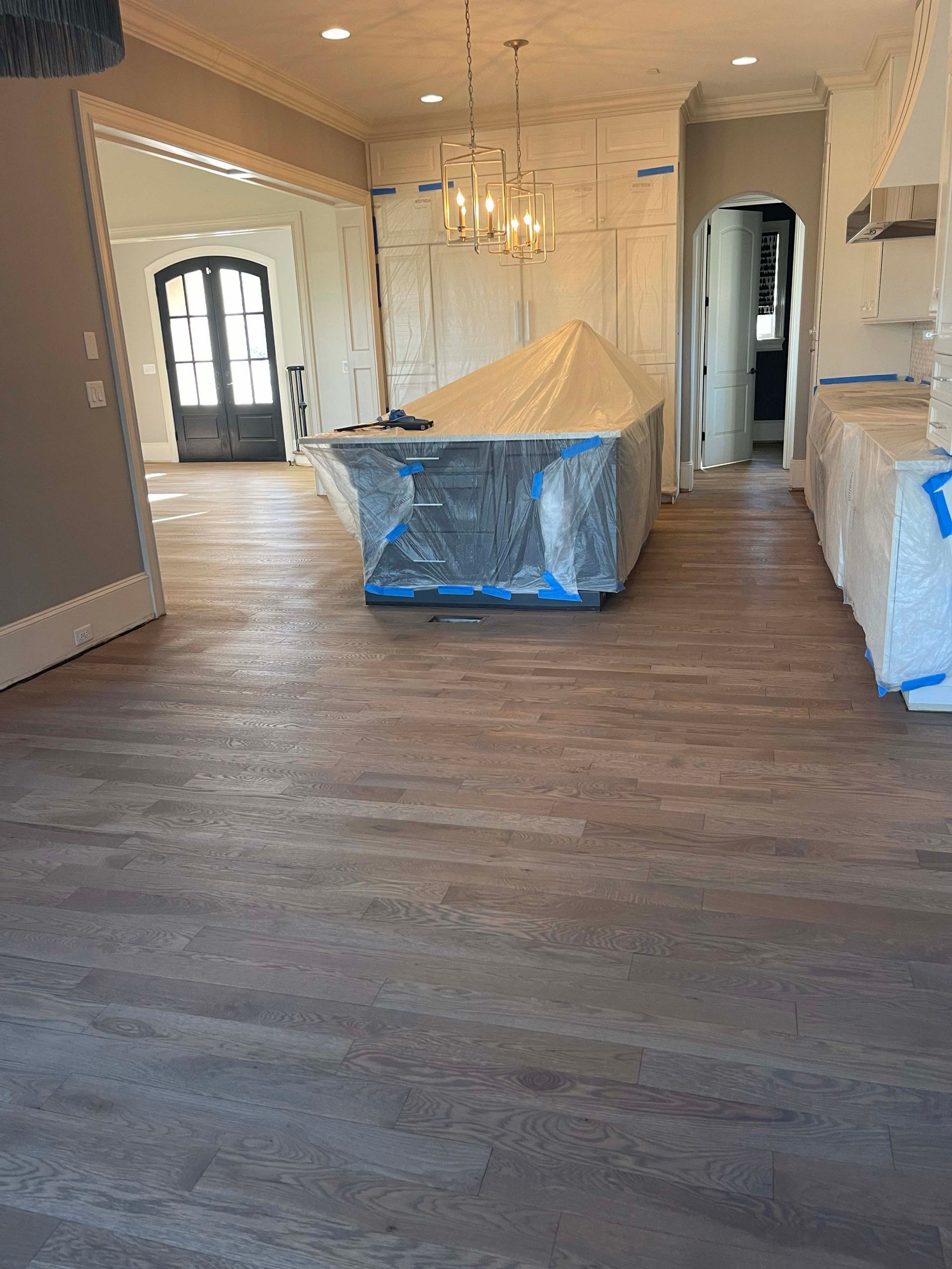 Kitchen with new wood-look flooring, island covered in plastic, and cabinets being worked on.