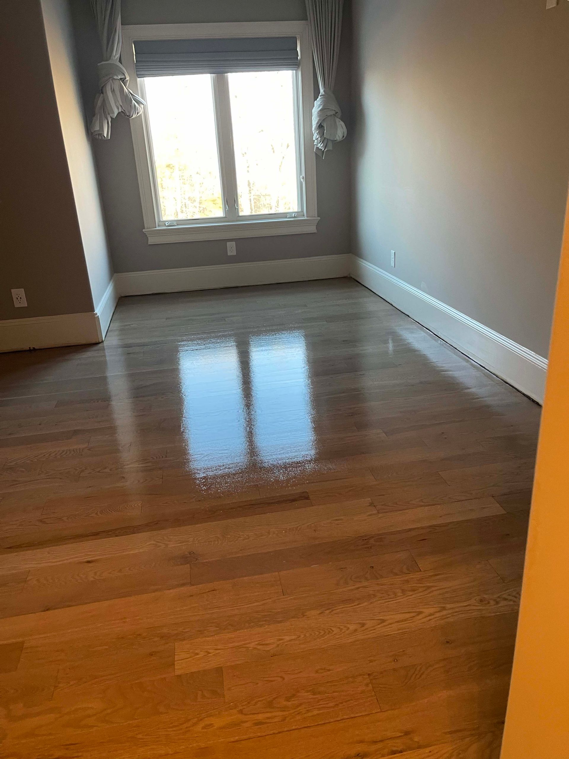Empty room with shiny hardwood floors and a window. Walls are neutral colors.