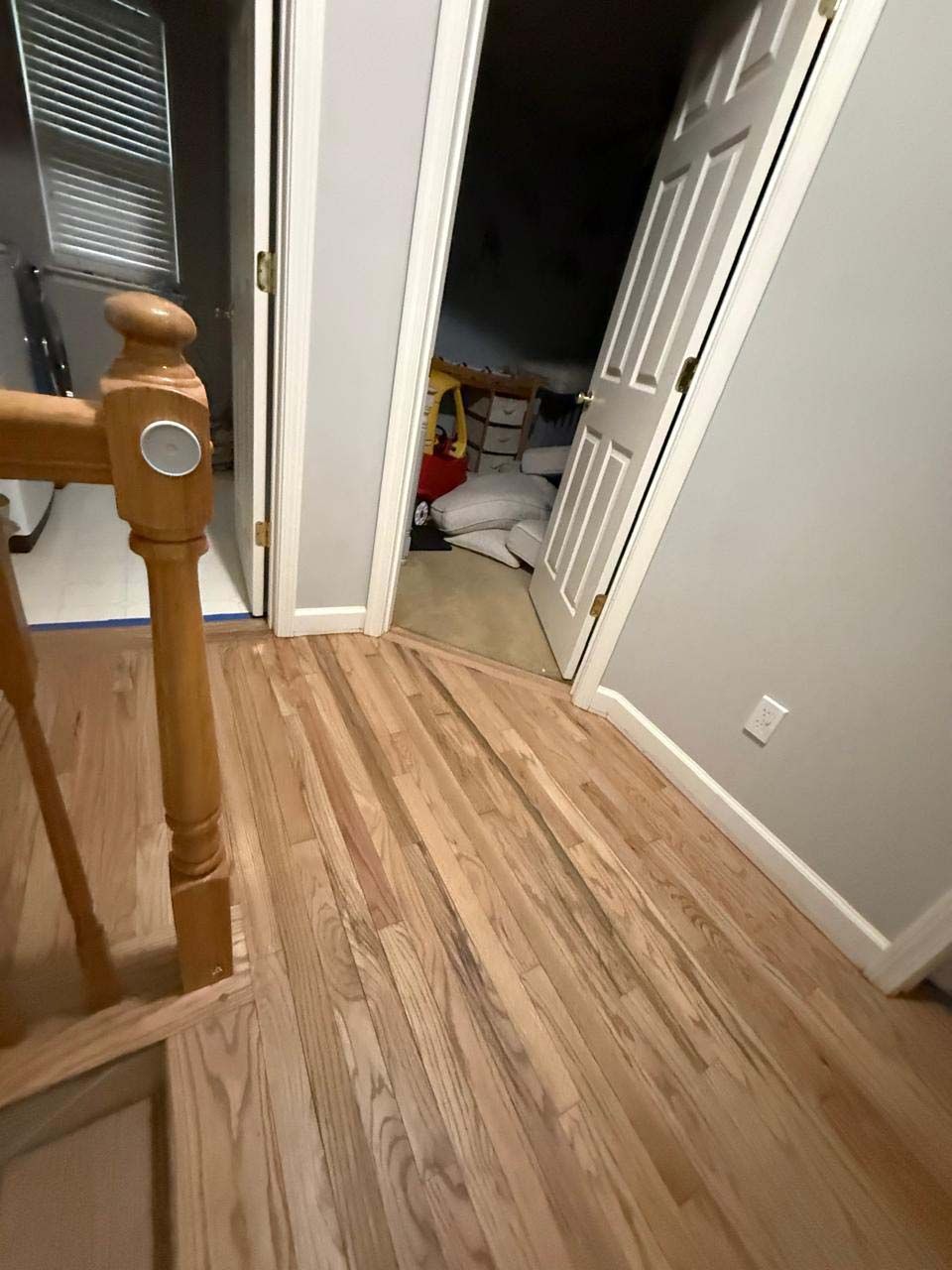 Wooden floor meets doorway with a slight slope. Closet doorway visible with items inside. Stair railing on the left.