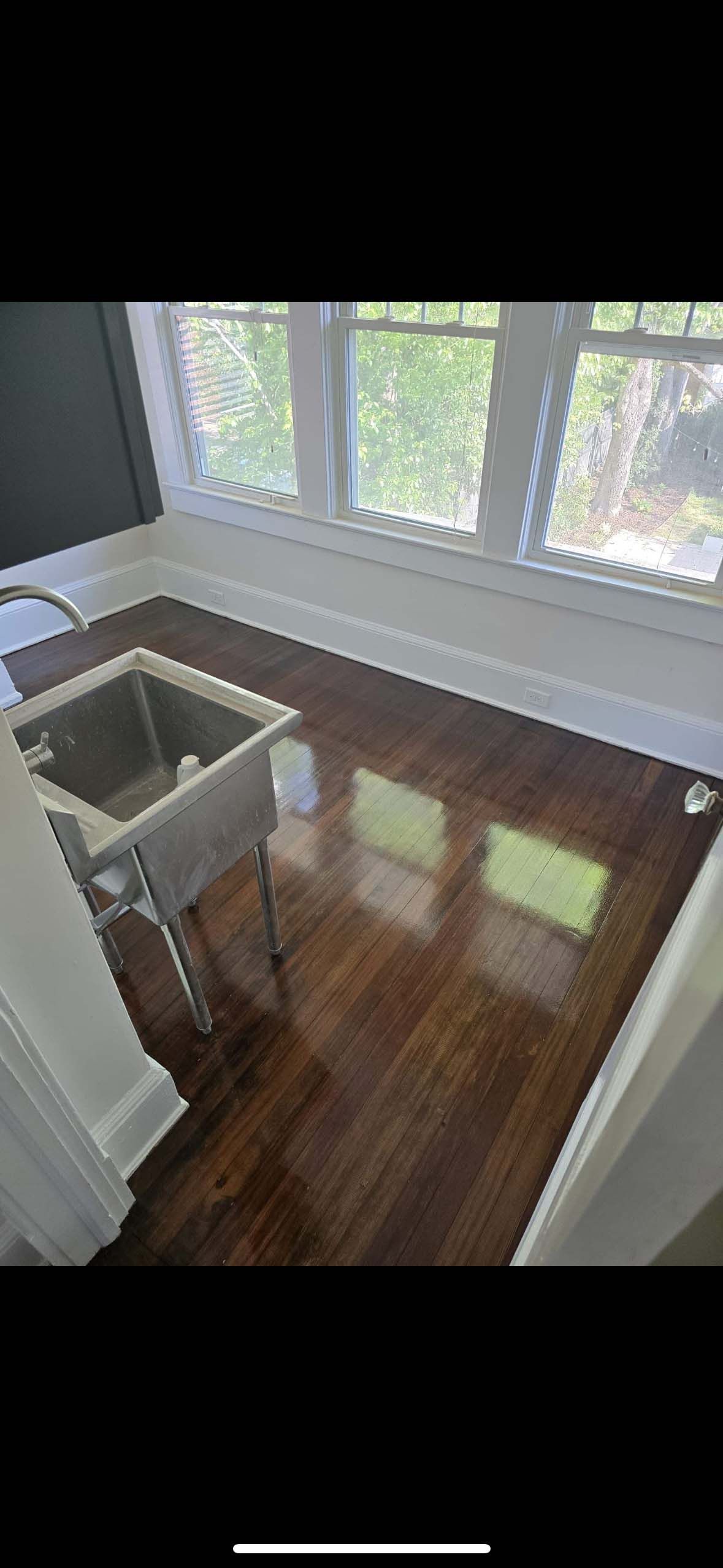 Dark hardwood floors in a room with a large window and a utility sink.