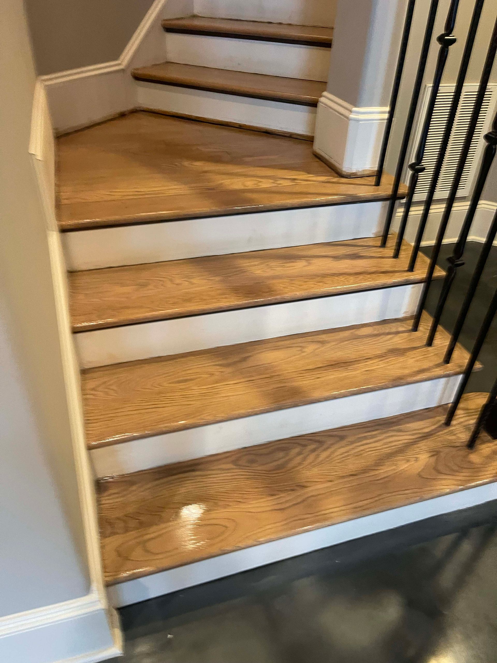 Wooden staircase with white trim, black metal railing, and gray walls.