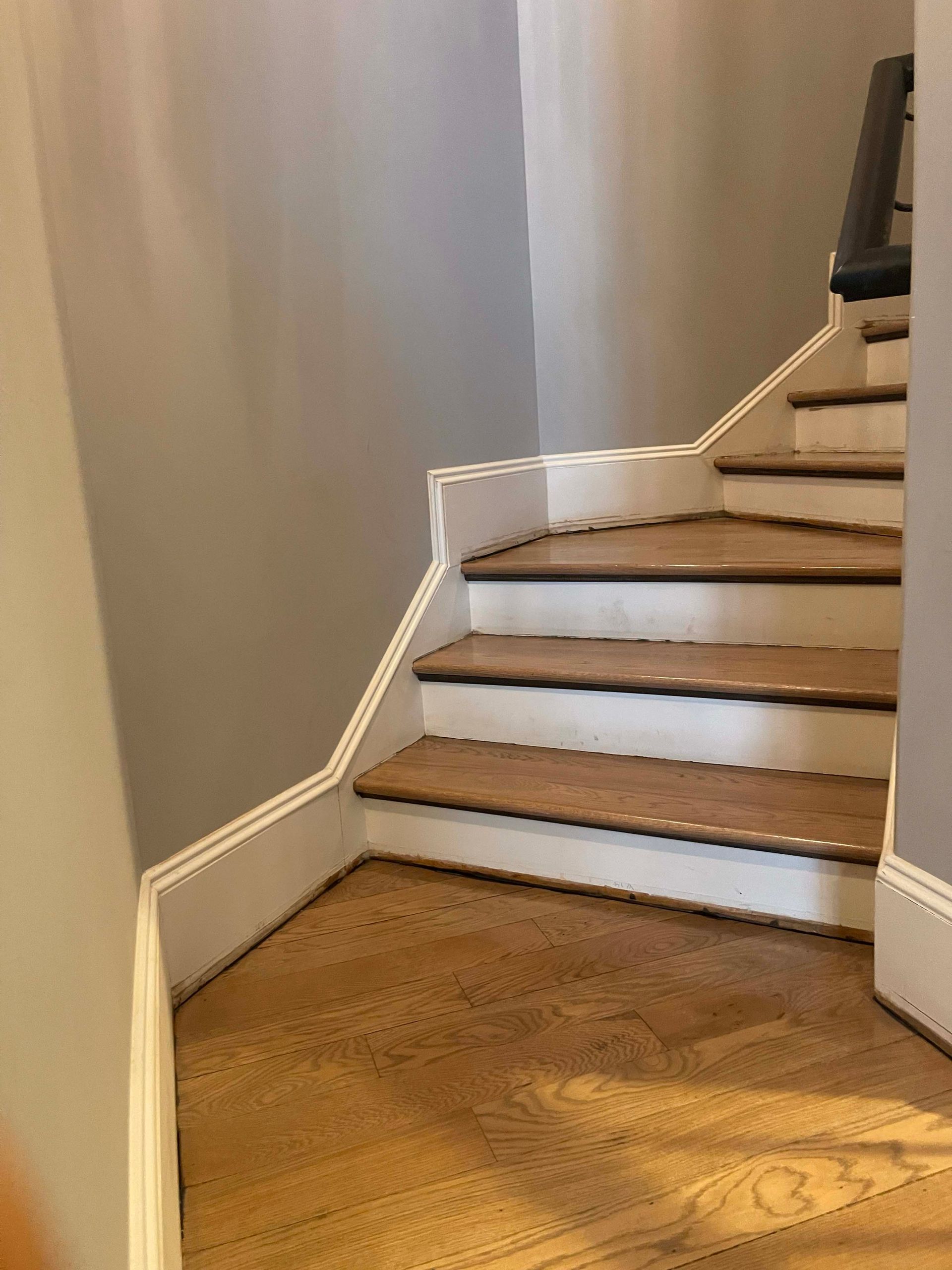 Staircase with wooden steps and white trim, leading upwards. Gray walls surround it.