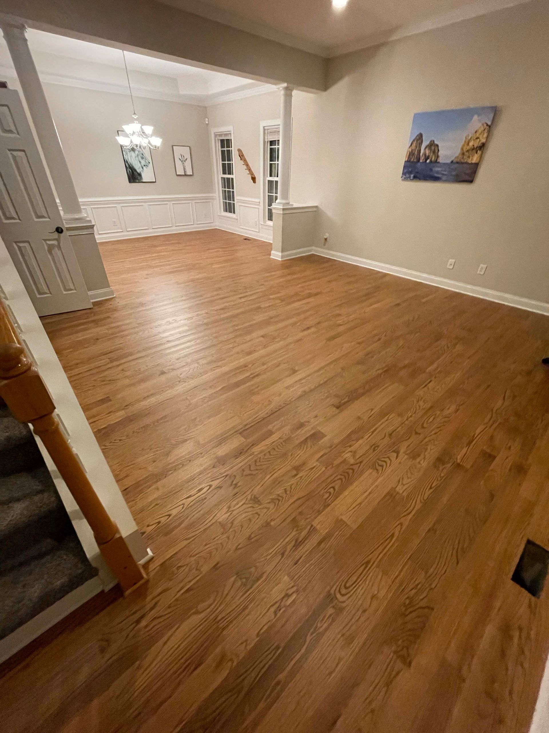 Hardwood floors in a home, leading to a dining area. Painting on wall, stairway on the left.