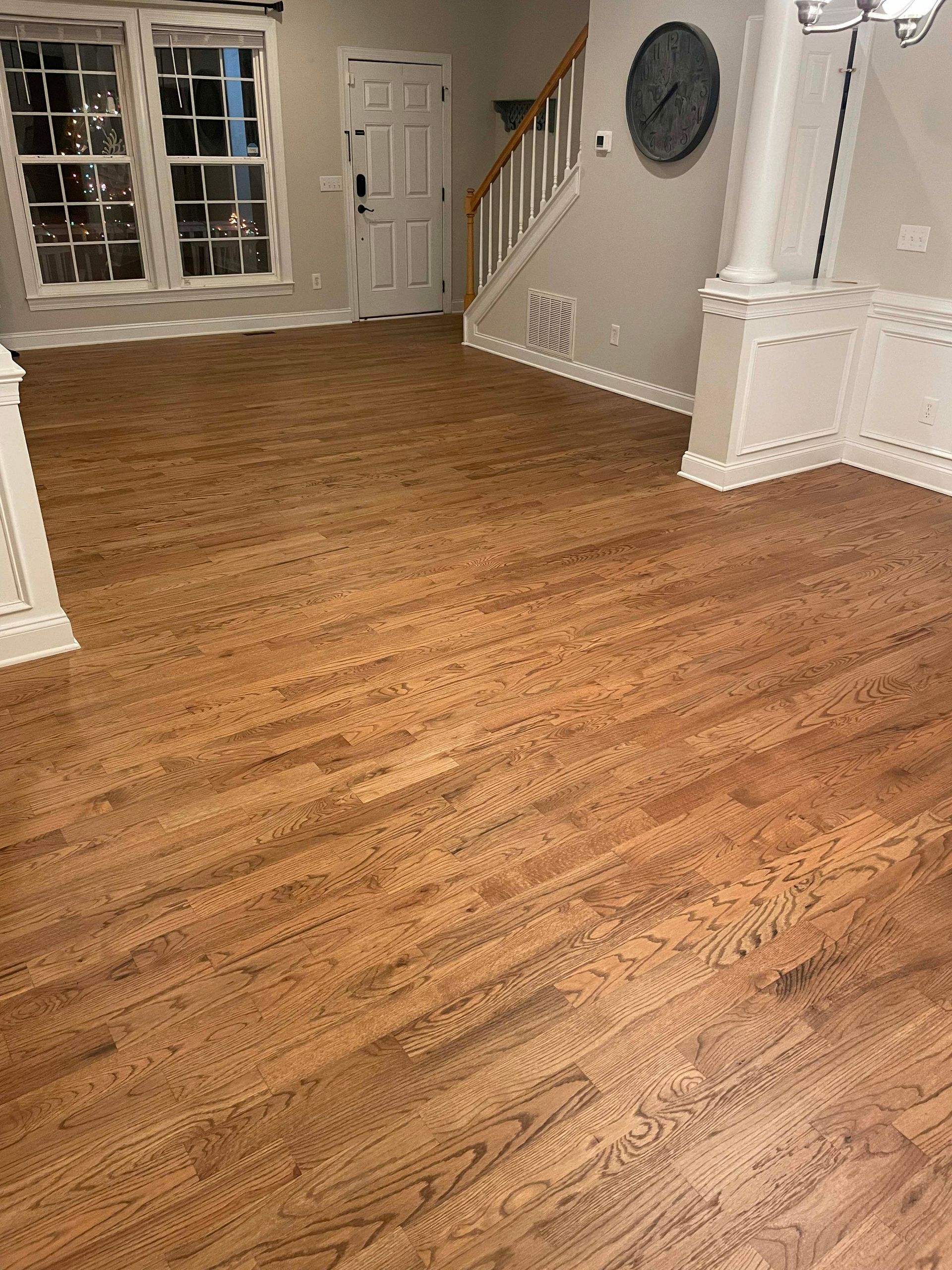 Wooden floors in an empty room, with white trim and a staircase, bathed in natural light.