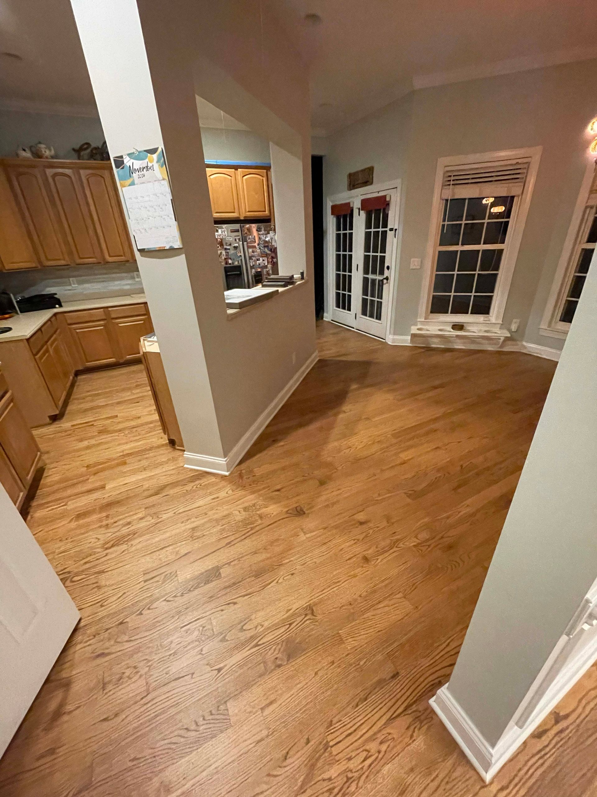 Hardwood floors in a home, transitioning to a kitchen area with light-colored cabinets.
