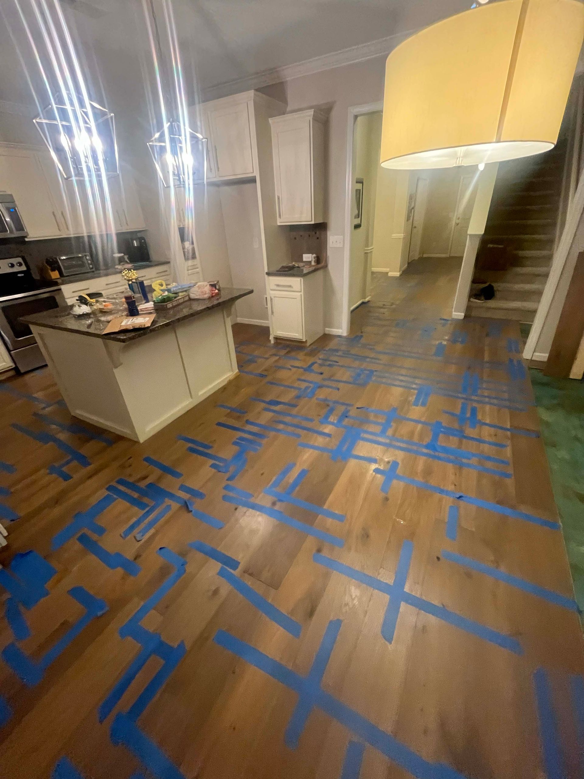 Hardwood floors covered in blue tape in a kitchen undergoing renovation; island and cabinets visible.