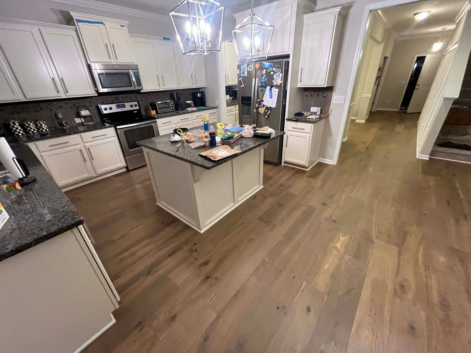 Kitchen with wood floors, island, white cabinets, stainless steel appliances, and a hallway entrance.