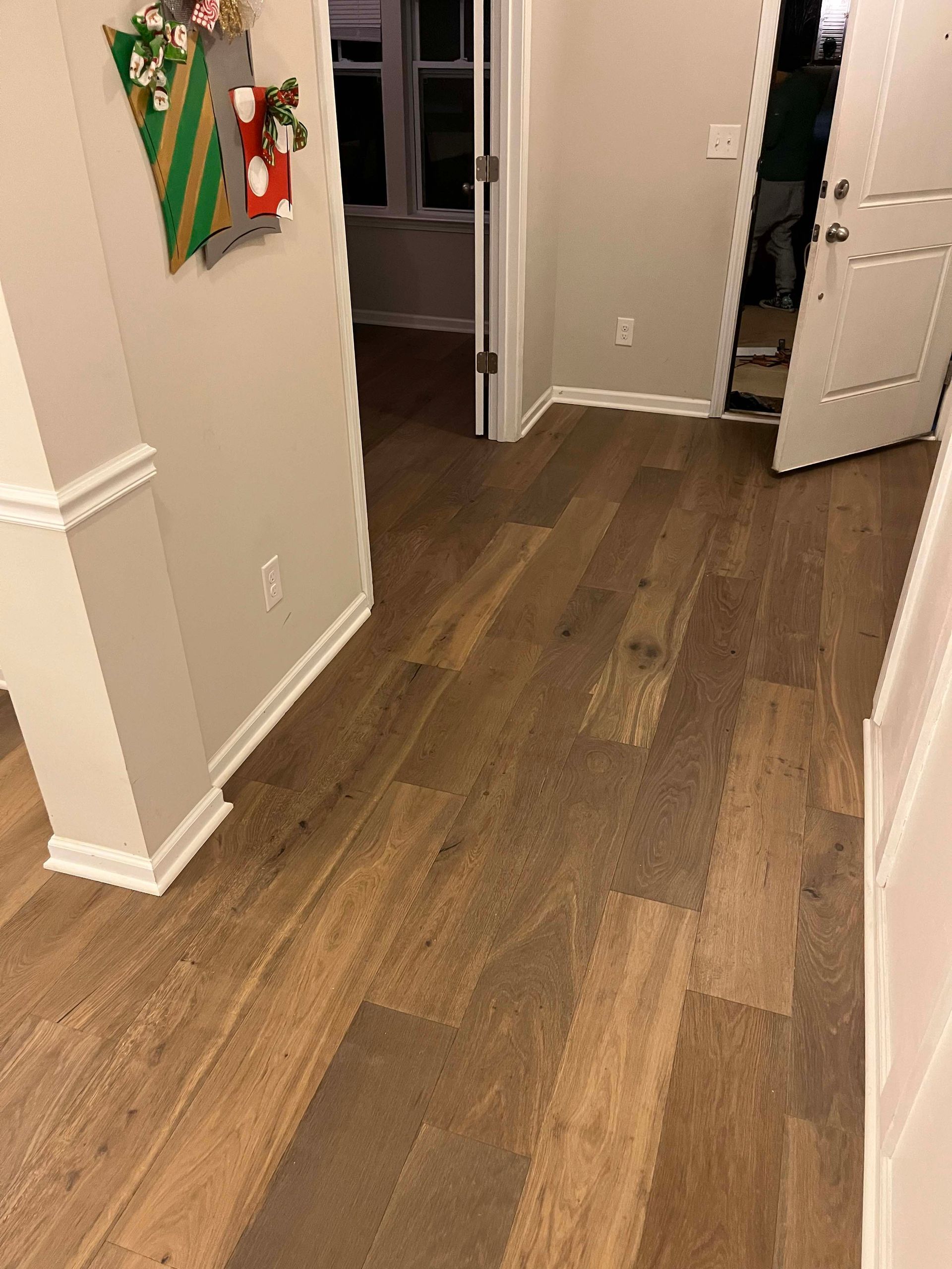 Wooden floor in a hallway with a door open to another room. A wall with a Christmas decoration is on the left.