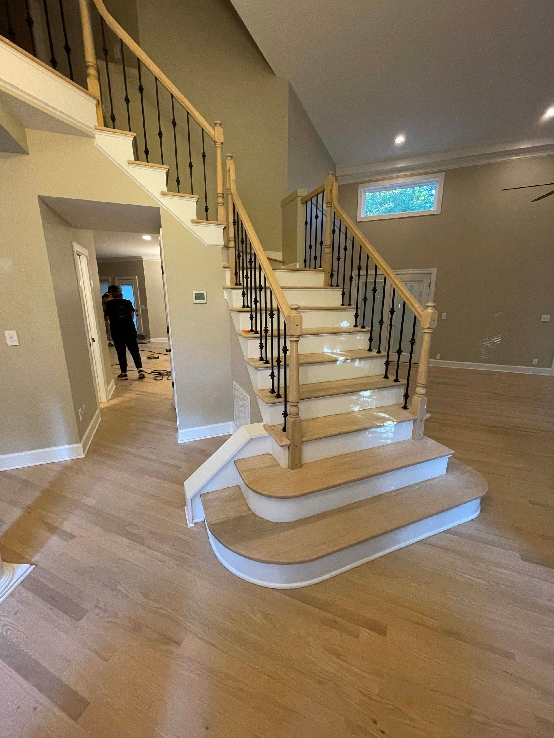 Staircase with light wood steps, black iron spindles, and light-colored railing. Person in doorway.
