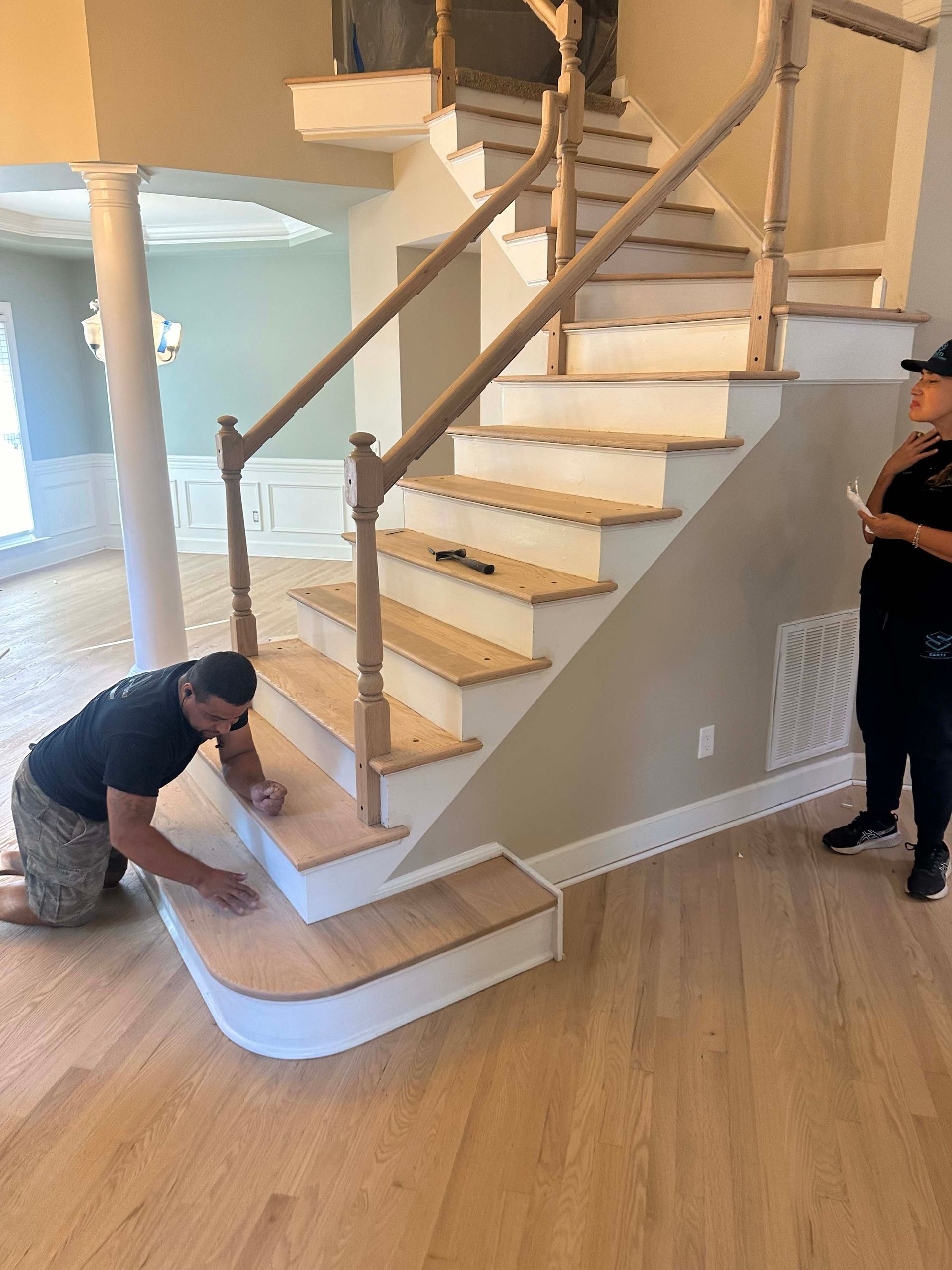 Two people installing wooden stairs in a home. One kneels, the other watches.